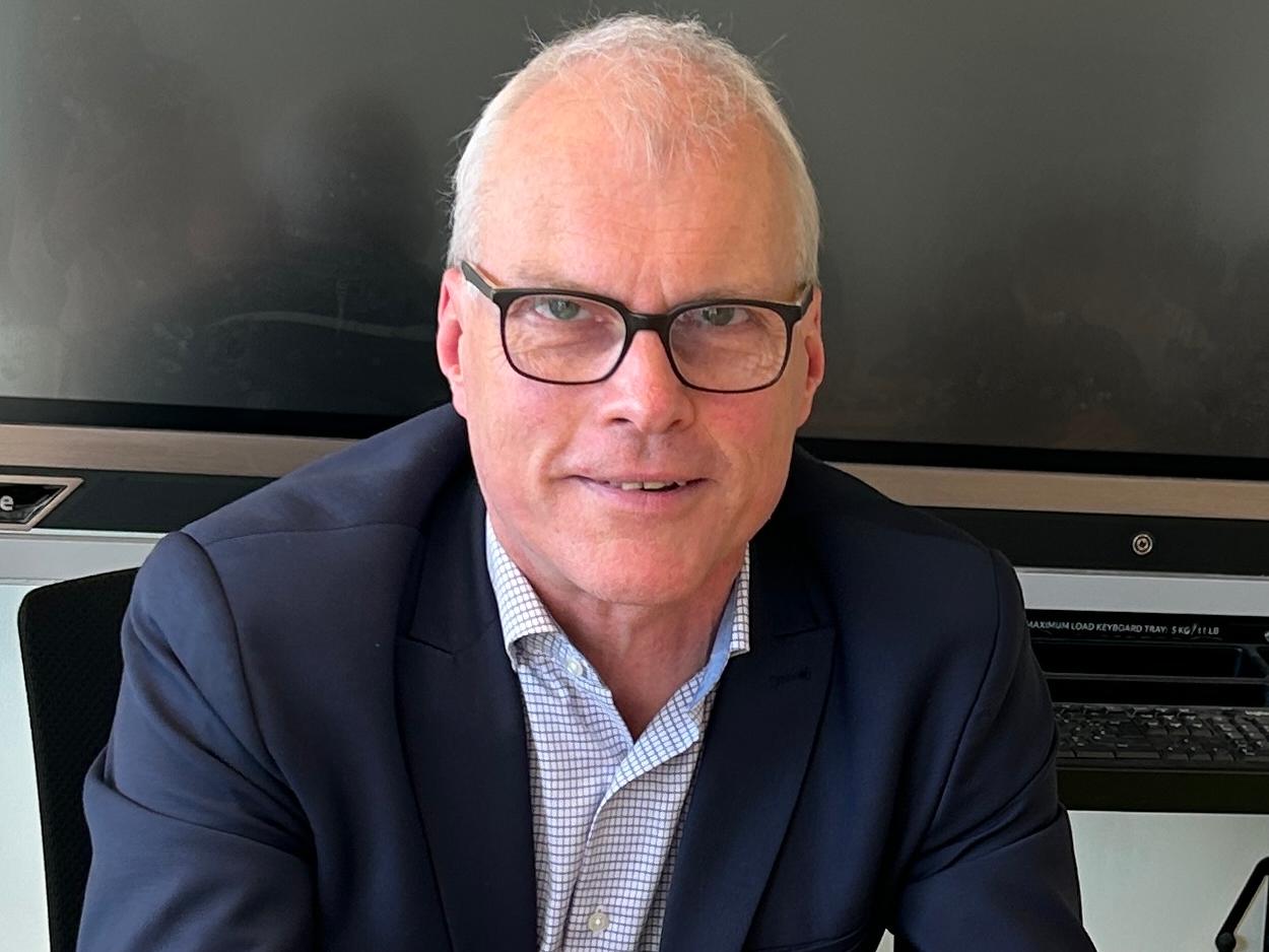 Mann sitzt im Klassenraum vor digitaler Tafel