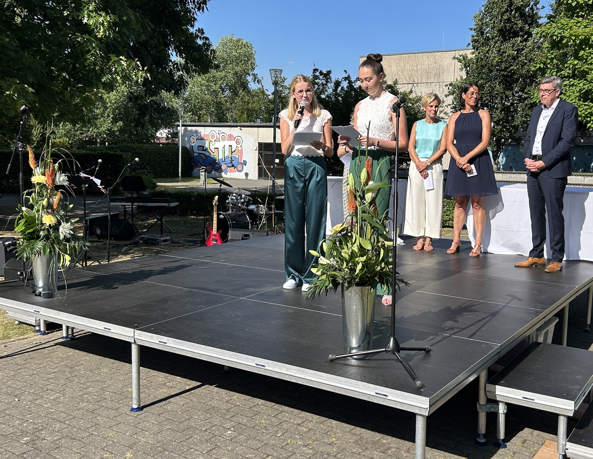 Schülerinnen auf der Bühne auf dem Schulhof, im Hintergrund Eltern und Lehrer:innen