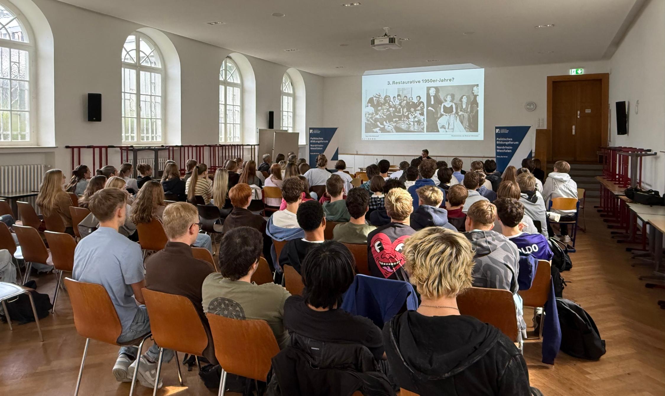 Schülerinnen und Schüler im Saal mit Blick auf den Vortragenden und die Leinwand