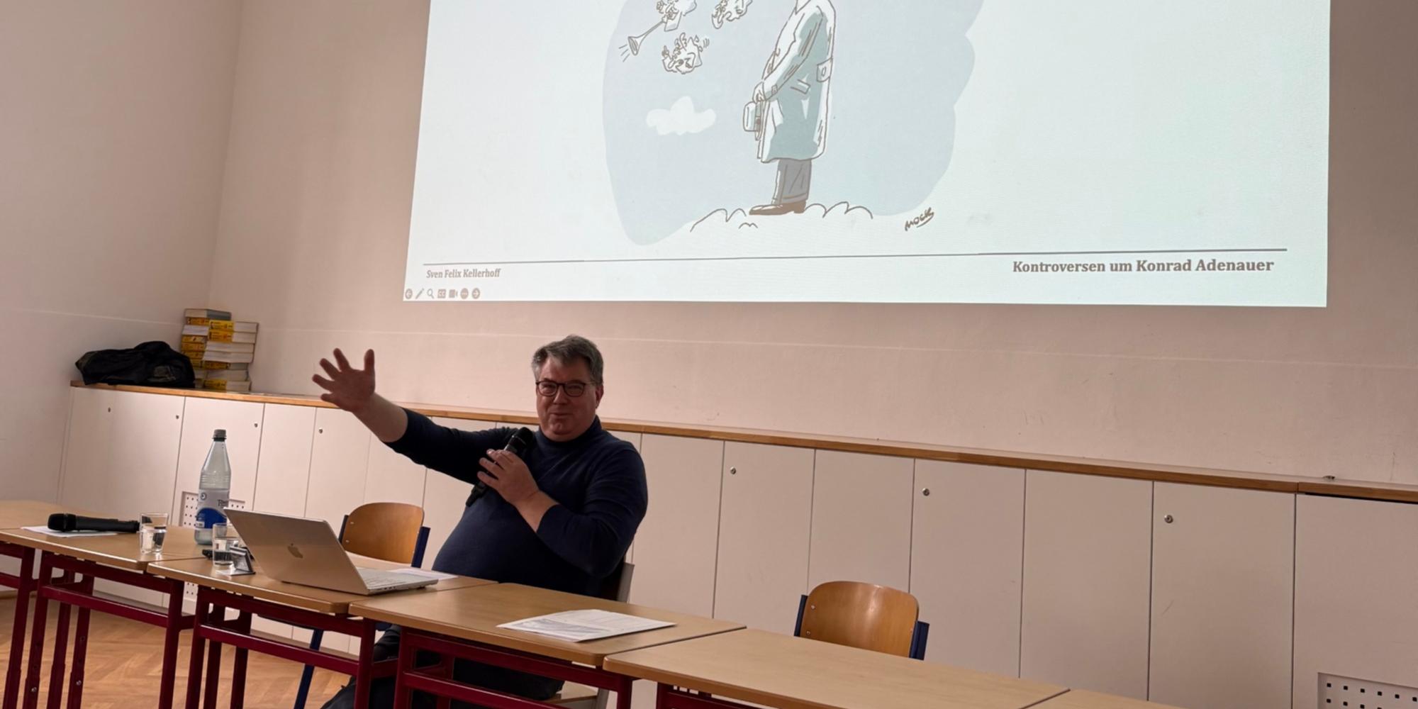 Vortragender sitzt vor Projektionsfläche mit Adenauer-Karikatur