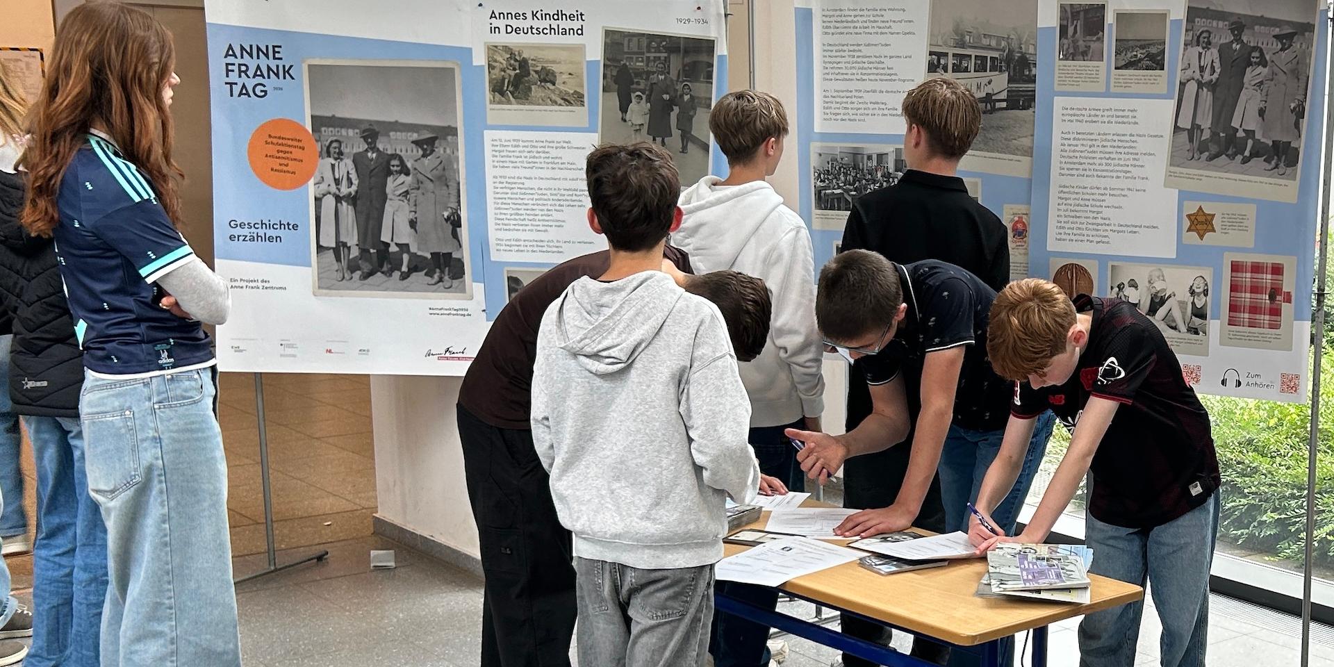 Schülerinnen und Schüler betrachten Ausstellungsplakate und sind über Arbeitsblätter gebeugt.