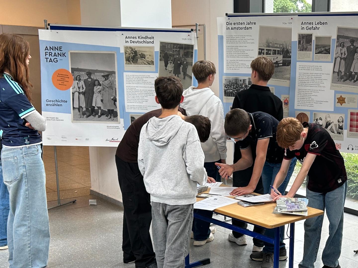 Schülerinnen und Schüler betrachten Ausstellungsplakate und sind über Arbeitsblätter gebeugt.
