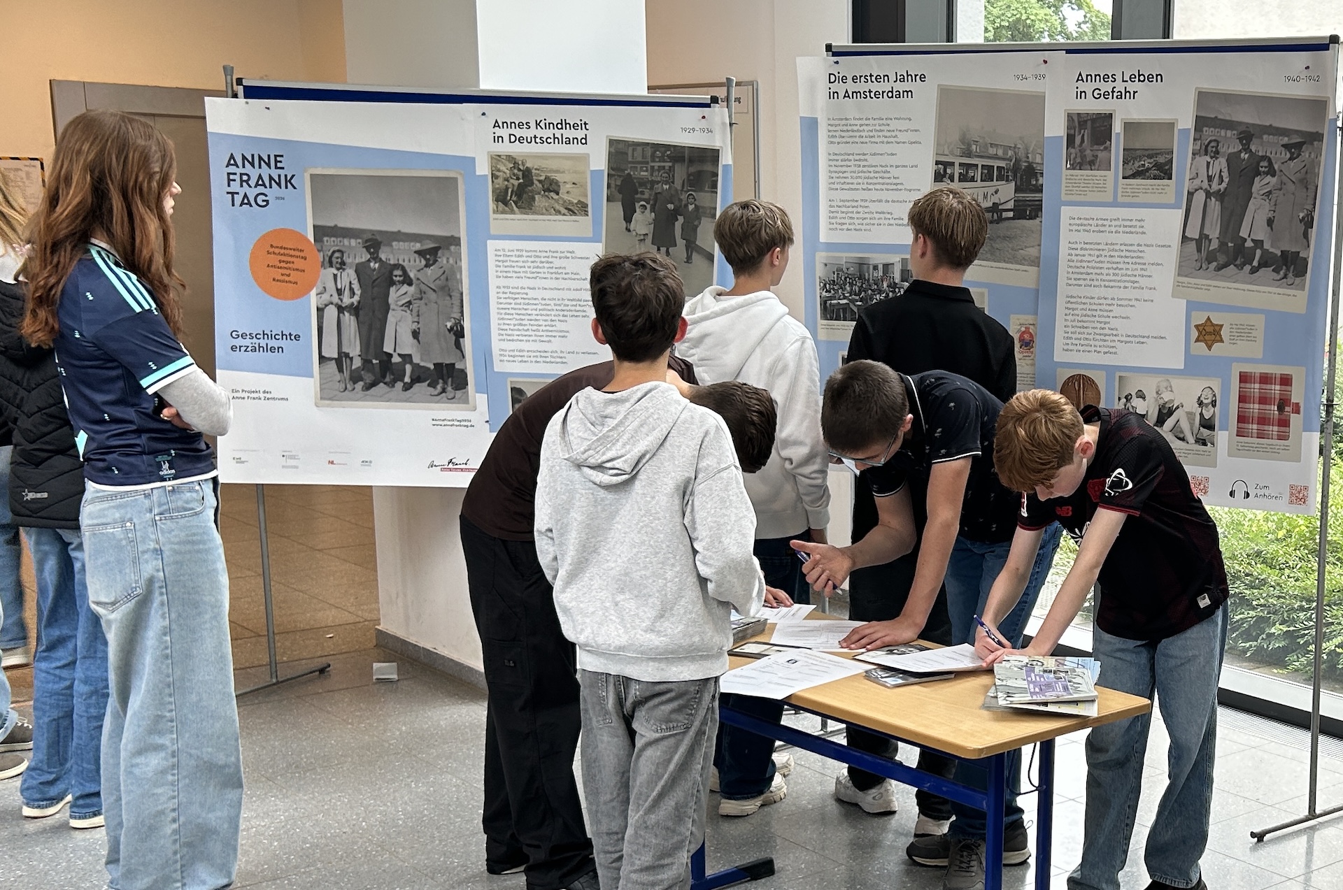 Schülerinnen und Schüler betrachten Ausstellungsplakate und sind über Arbeitsblätter gebeugt.