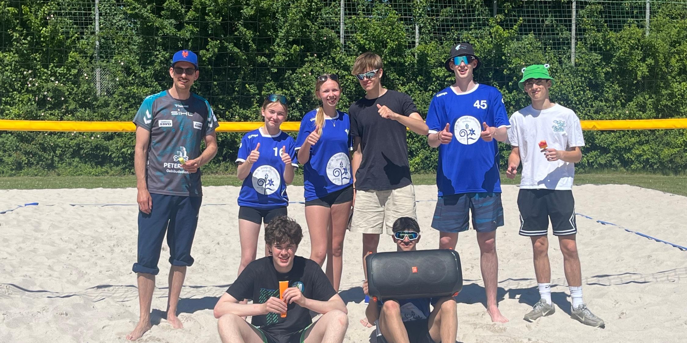 Beachvolleyball-Damen und -Herren mit Lehrer im Sand vor dem Netz
