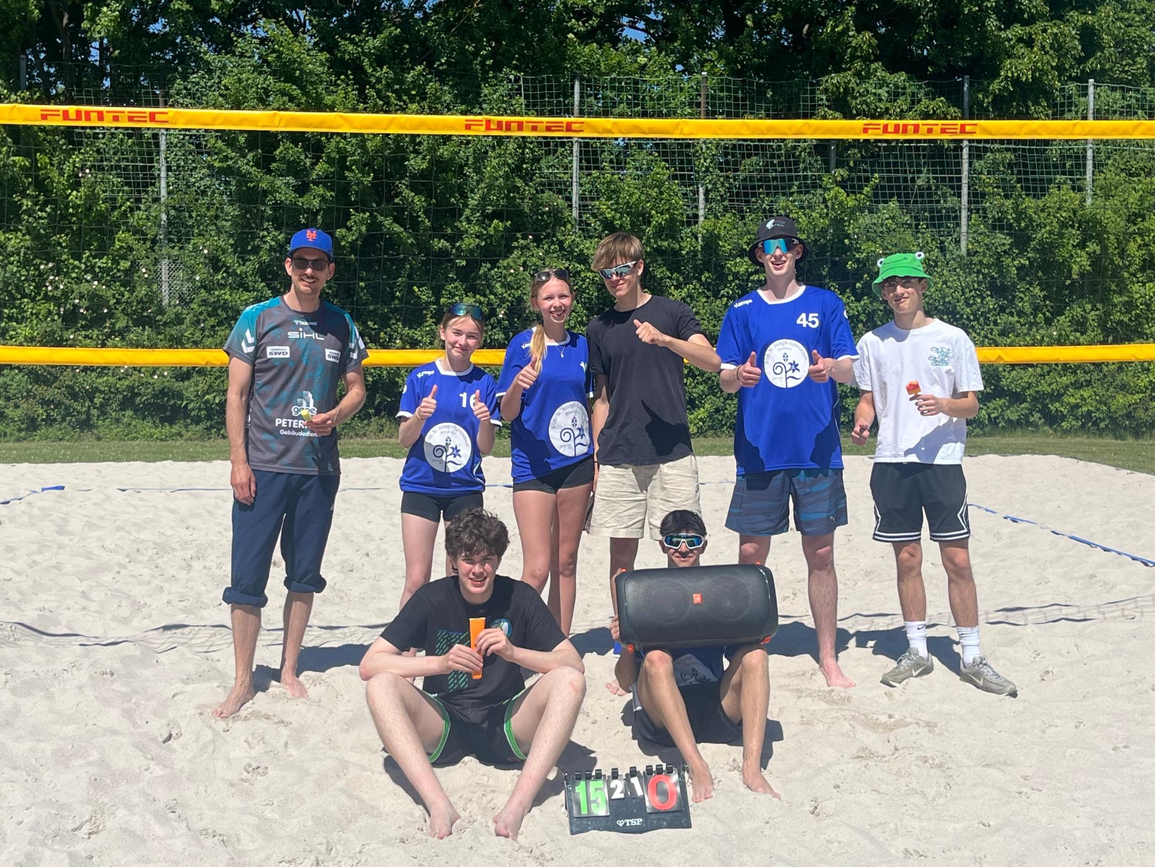 Beachvolleyball-Damen und -Herren mit Lehrer im Sand vor dem Netz