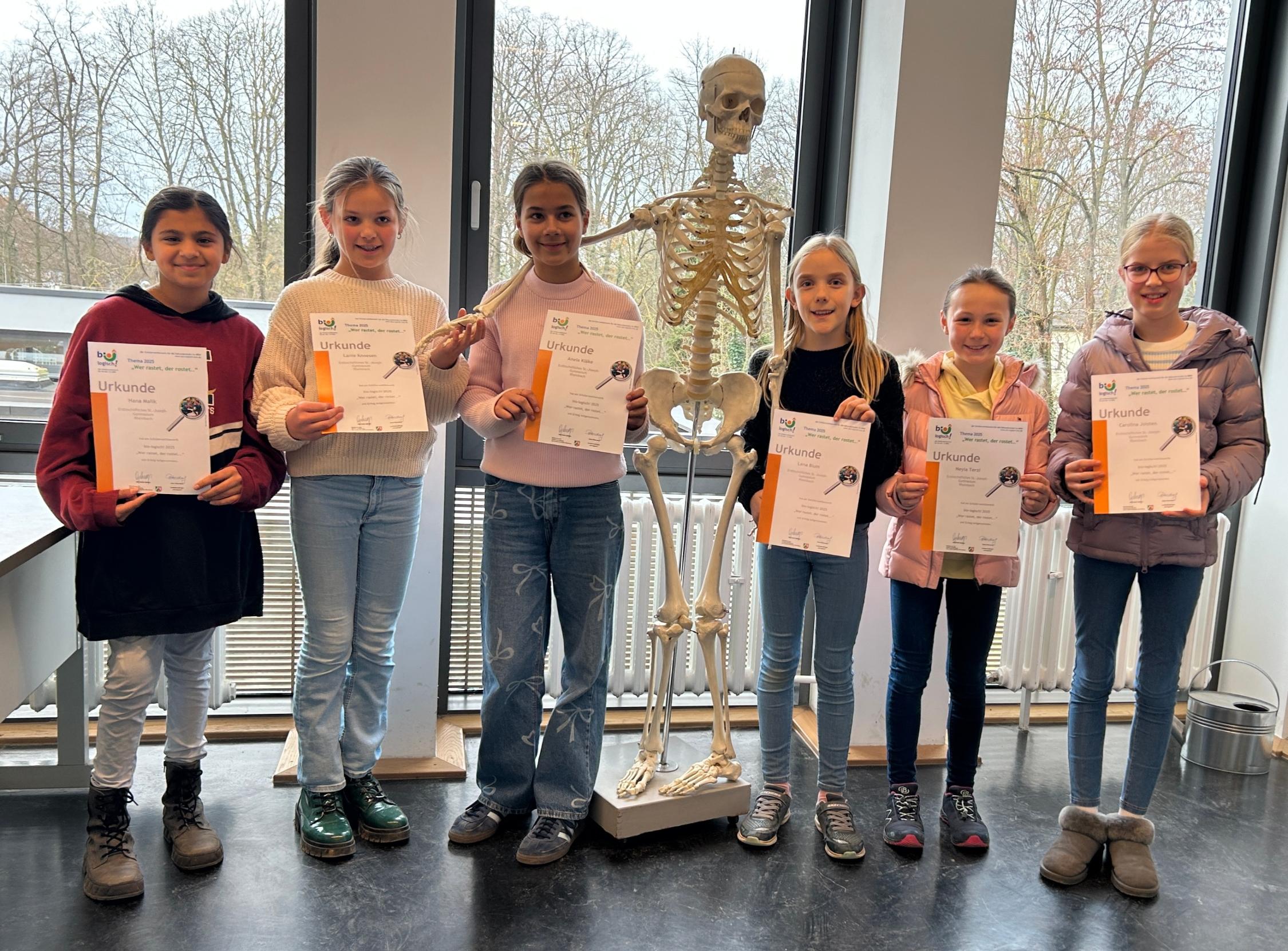 Schülerinnen mit Urkunden in der Hand, im Hintergrund ein Skelett