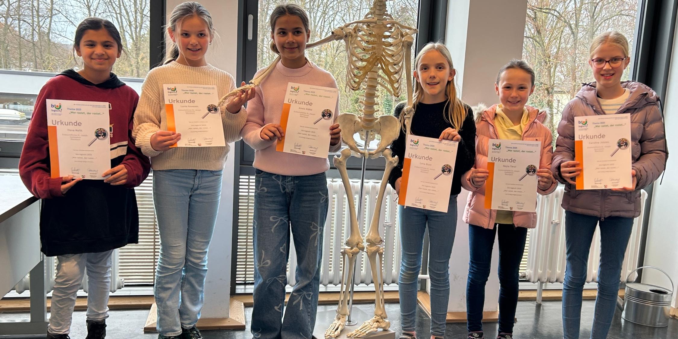 Schülerinnen mit Urkunden in der Hand, im Hintergrund ein Skelett