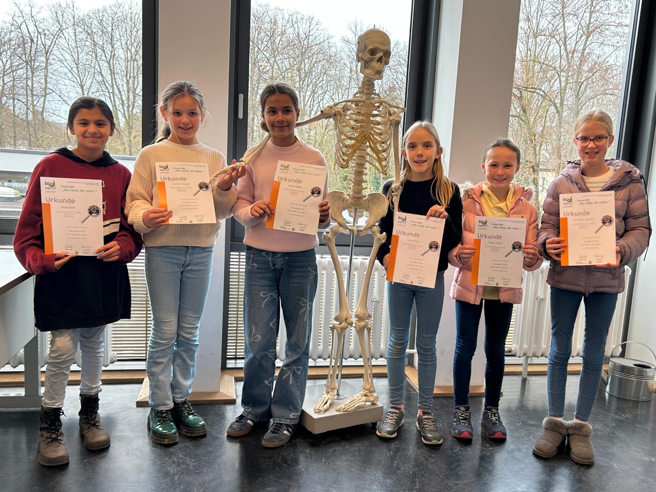 Schülerinnen mit Urkunden in der Hand, im Hintergrund ein Skelett