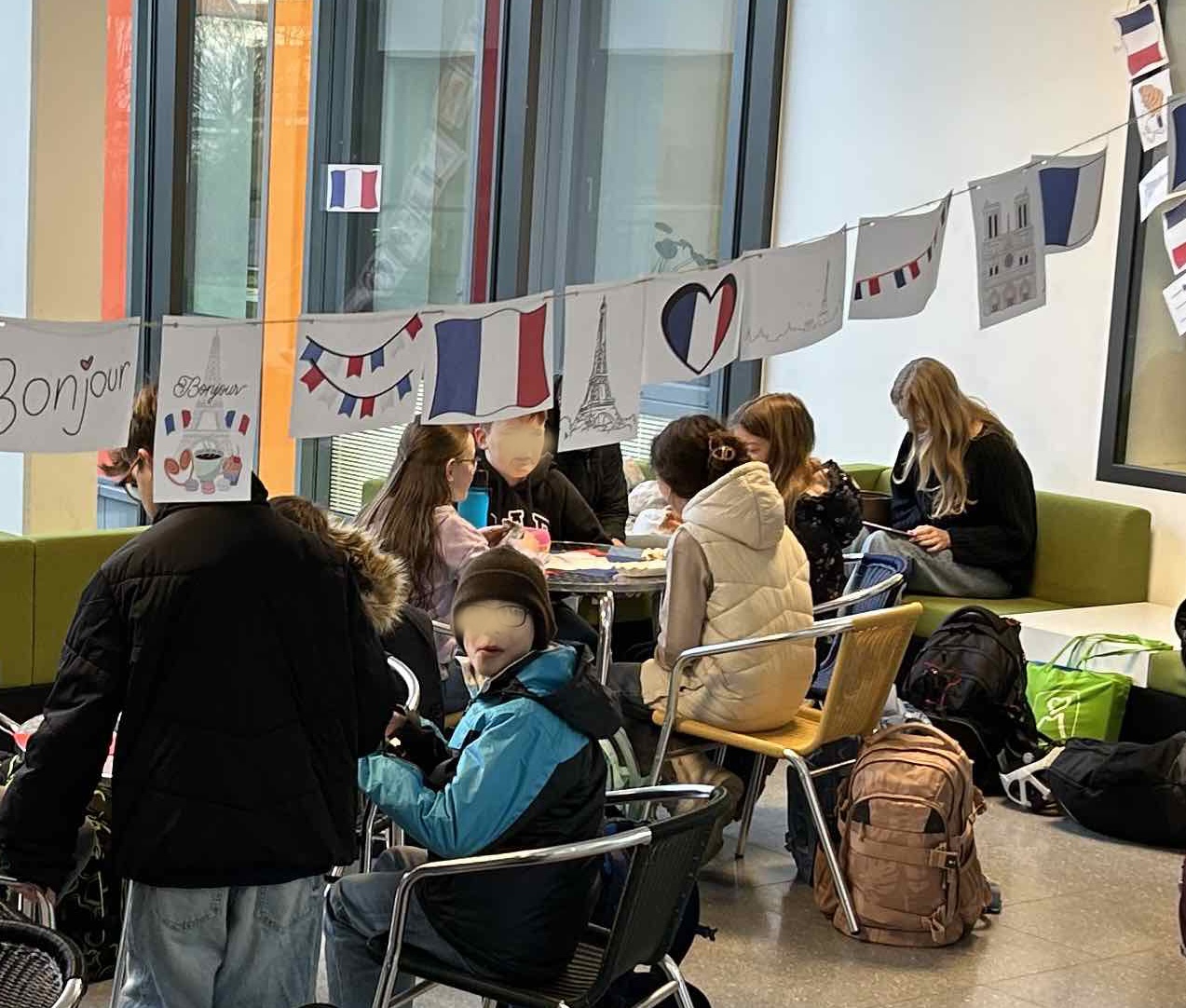Schüler:inen sitzen auf Stühlen und Sofas, Girlande mit Frankreich-Motiven