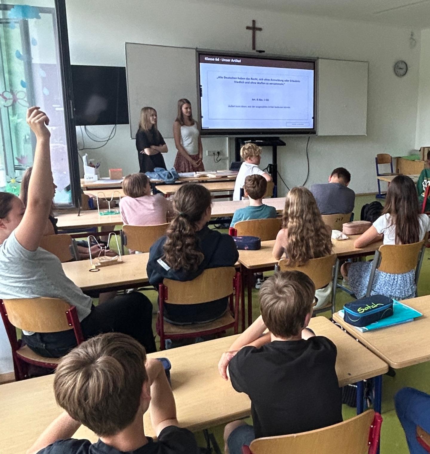 zwei Schülerinnen stehen vor einer Schulklasse