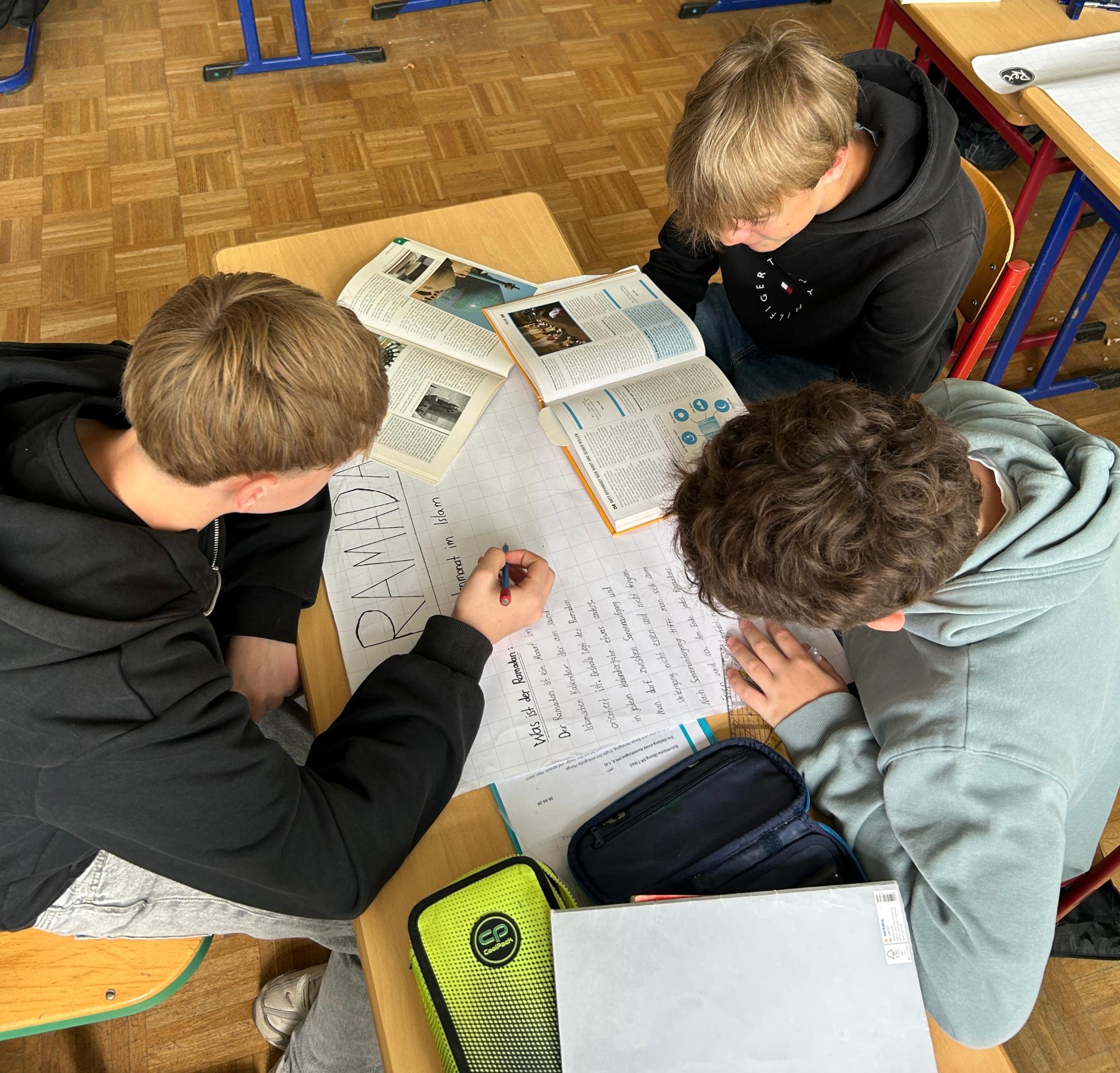 drei Jungen bei einer Gruppenarbeit: aufgeklappte Bücher, Plakat mit der Überschrift 'Ramadan'