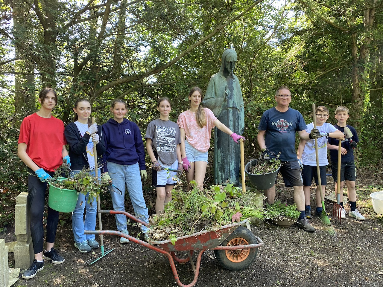 Schülerinnen und Schüler sowie Eltern auf dem Friedhof mit Gartengeräten und Schubkarre