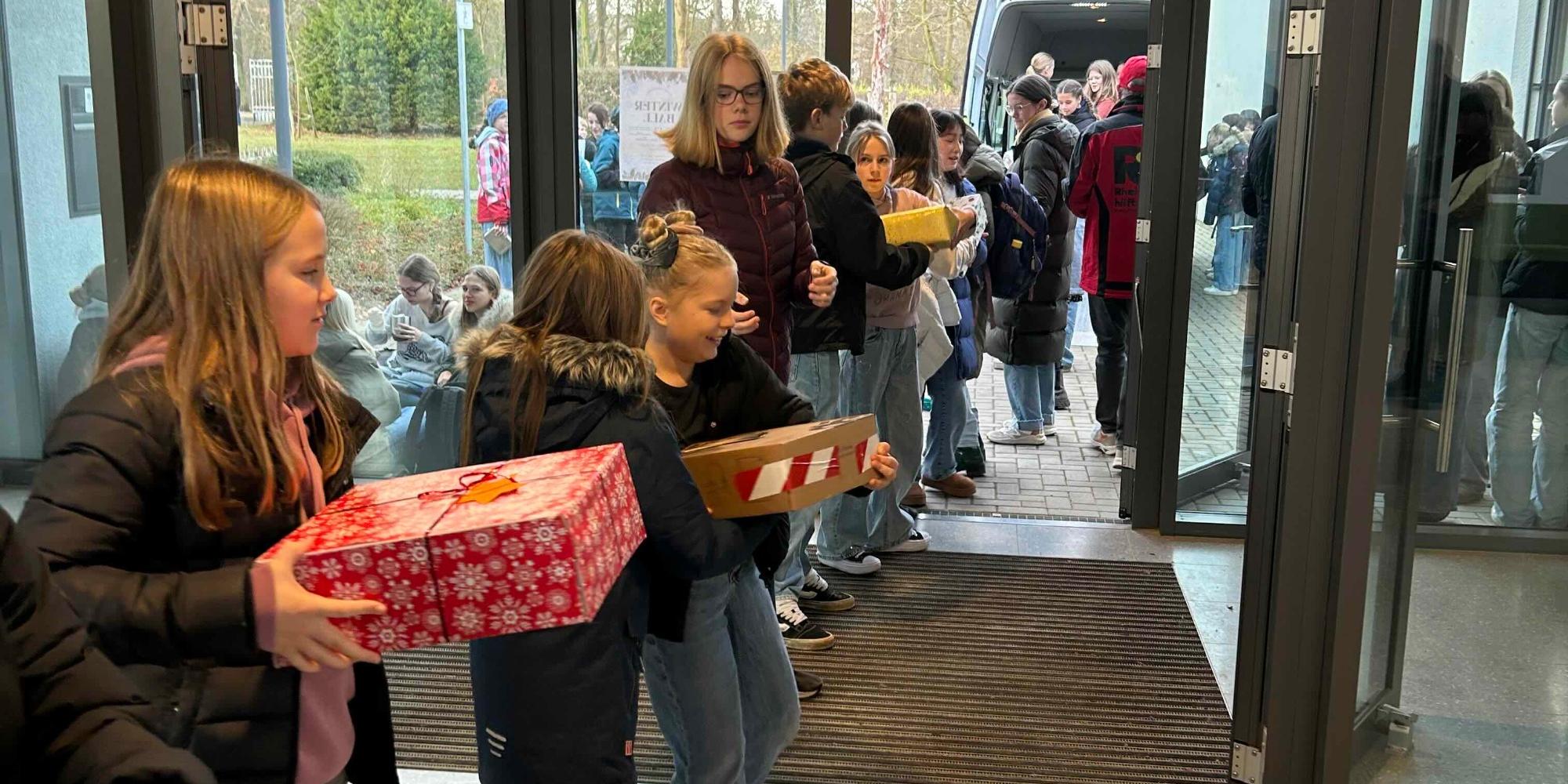Schüler:innen geben eingepackte Geschenke von Hand zu Hand bis zum Lkw