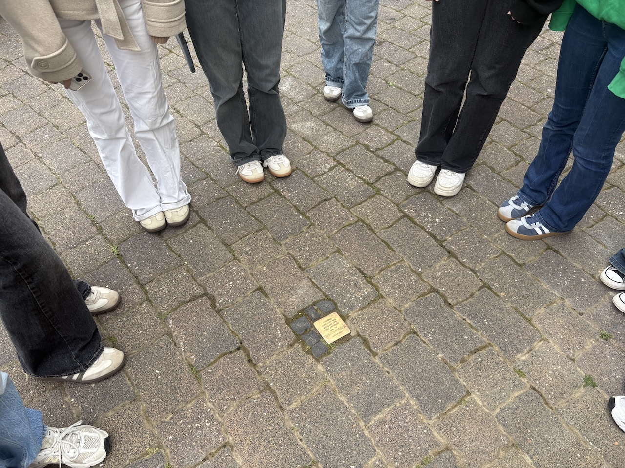 Stolperstein in der Mitte, um ihn herum Füße und Beine