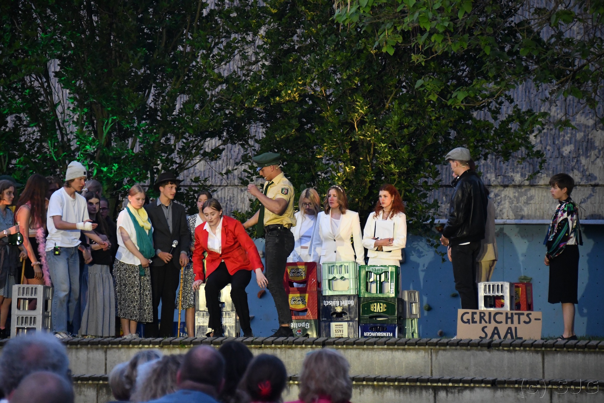 Open-Air-Bühne mit Schauspieler:innen in Chantals Kiosk, Mr. Jones vorn