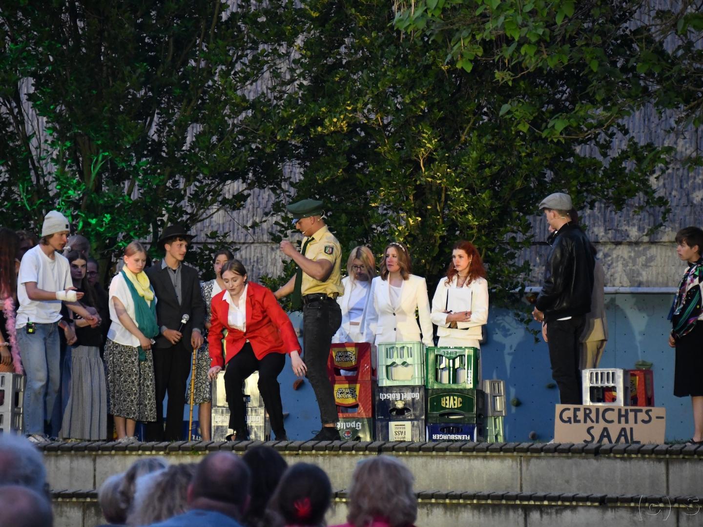 Open-Air-Bühne mit Schauspieler:innen in Chantals Kiosk, Mr. Jones vorn