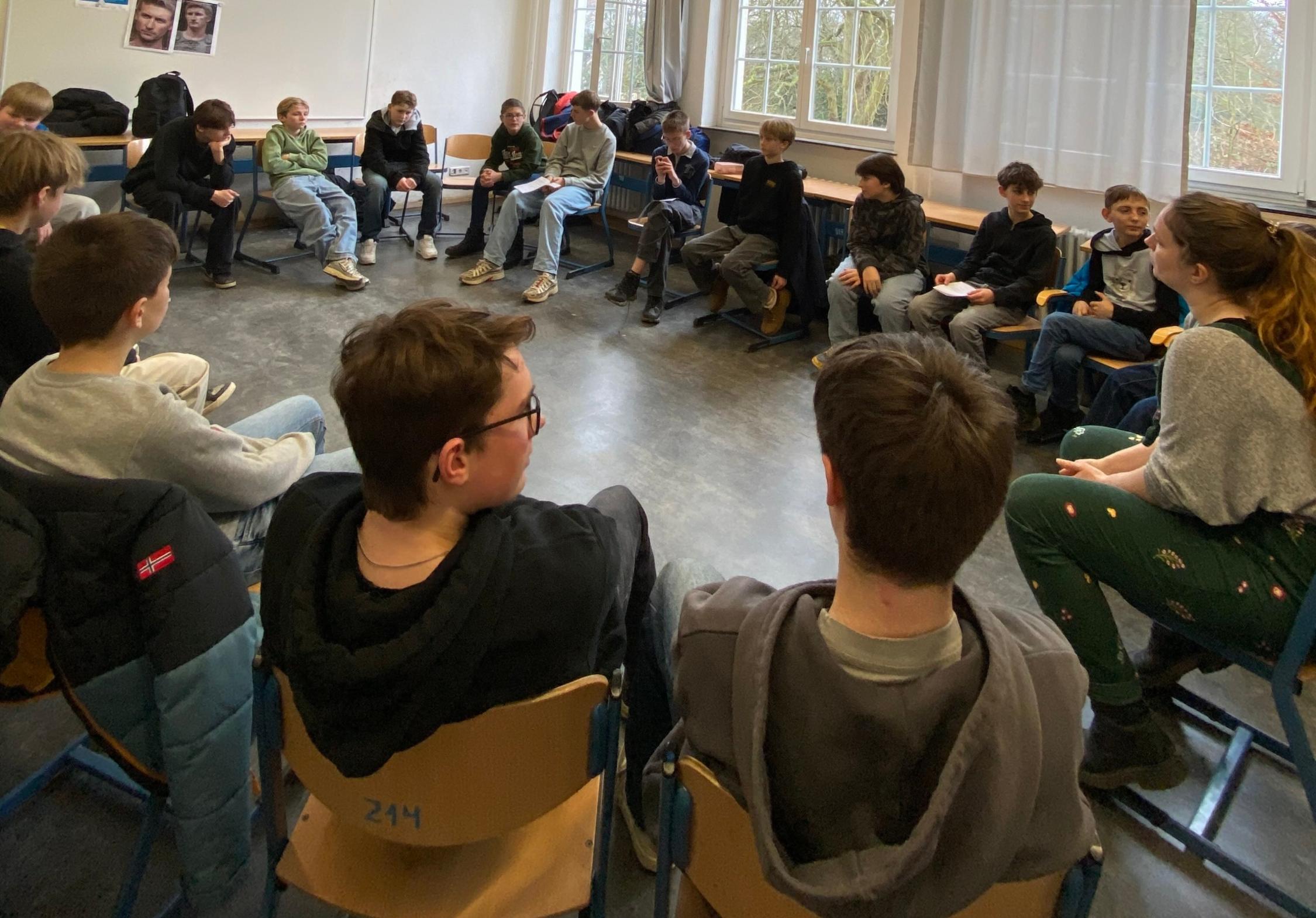 Jungen sitzen im Stuhlkreis, eine Frau spricht