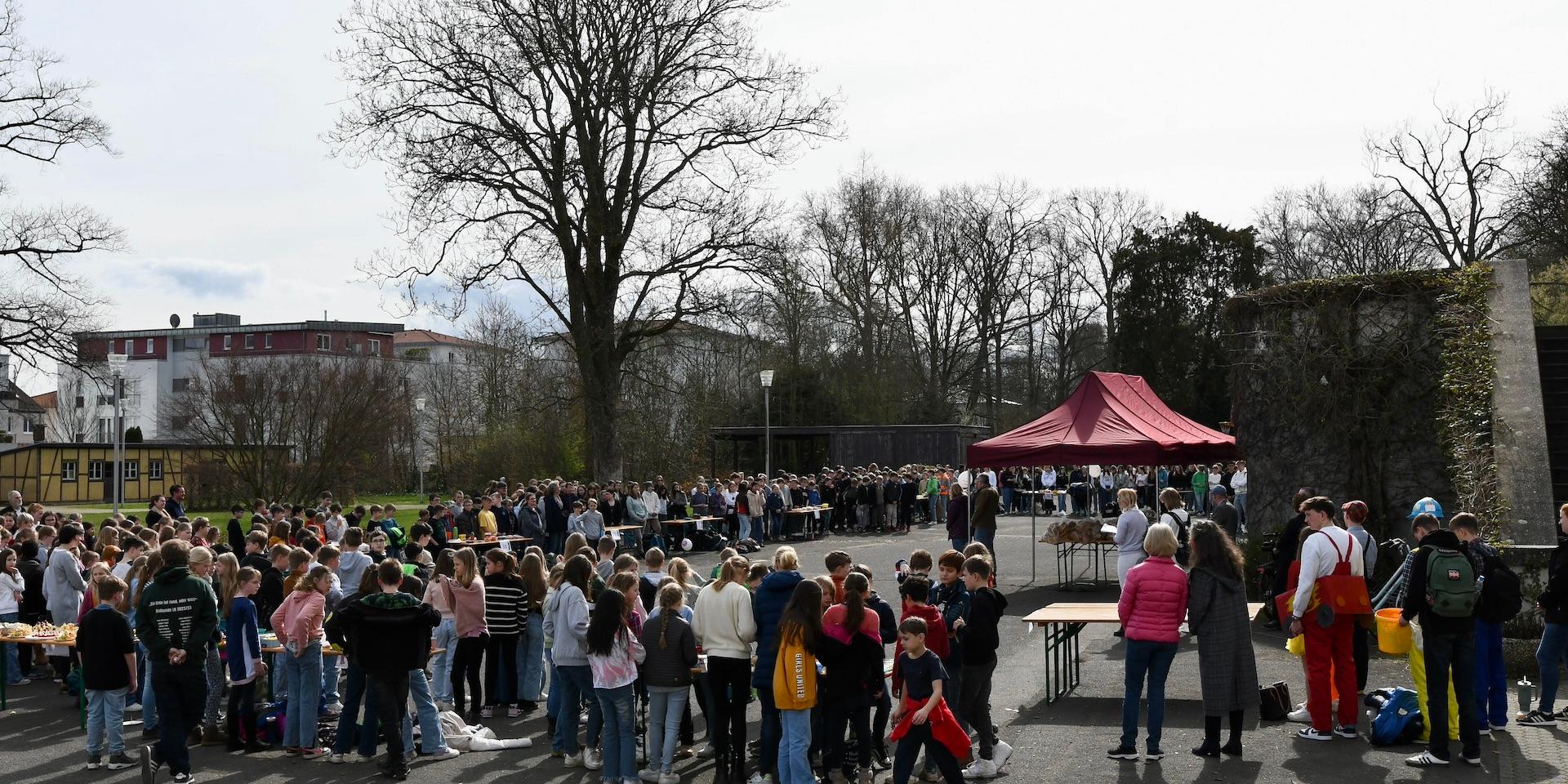 Schulgemeinschaft vor Tischen auf dem Schulhof, Pfarrer am Mikrofon