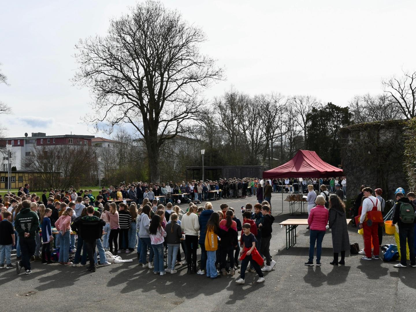 Schulgemeinschaft vor Tischen auf dem Schulhof, Pfarrer am Mikrofon