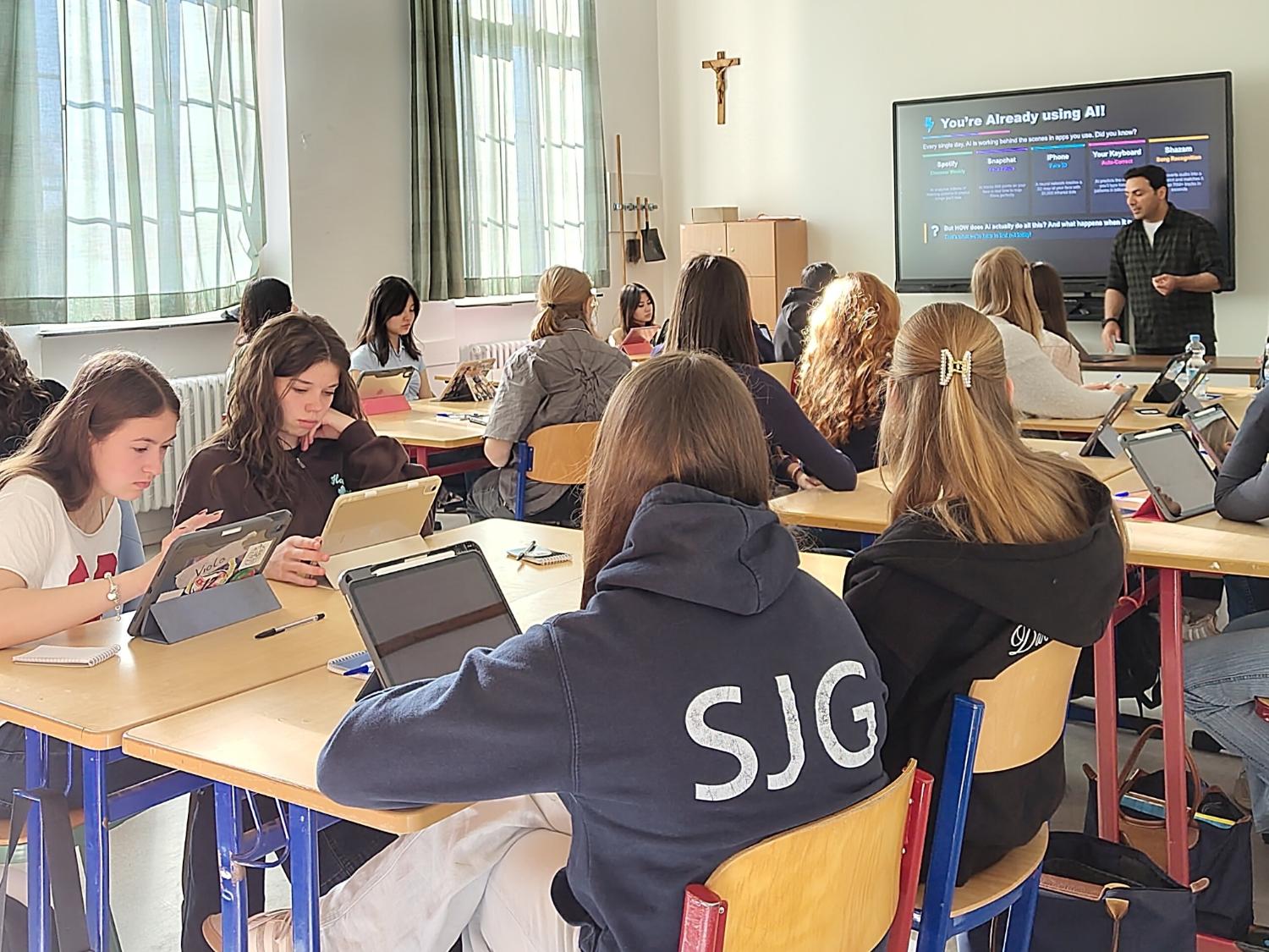 Schülerinnen in einem Klassenraum, Mann vor digitaler Tafel