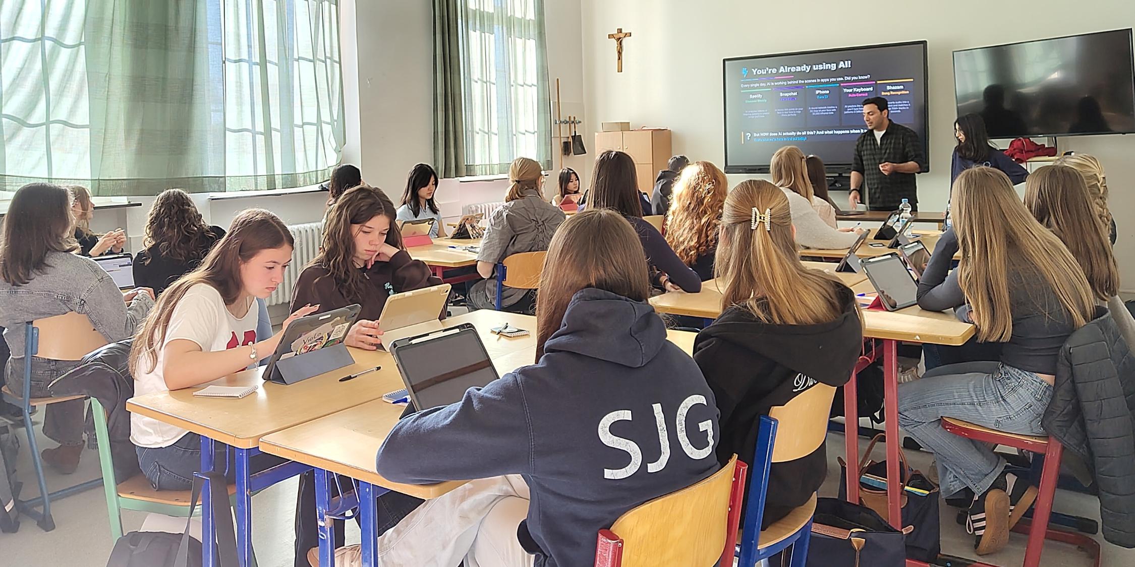 Schülerinnen in einem Klassenraum, Mann vor digitaler Tafel