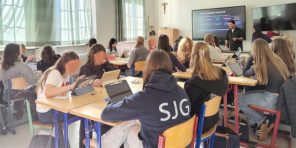 Schülerinnen in einem Klassenraum, Mann vor digitaler Tafel