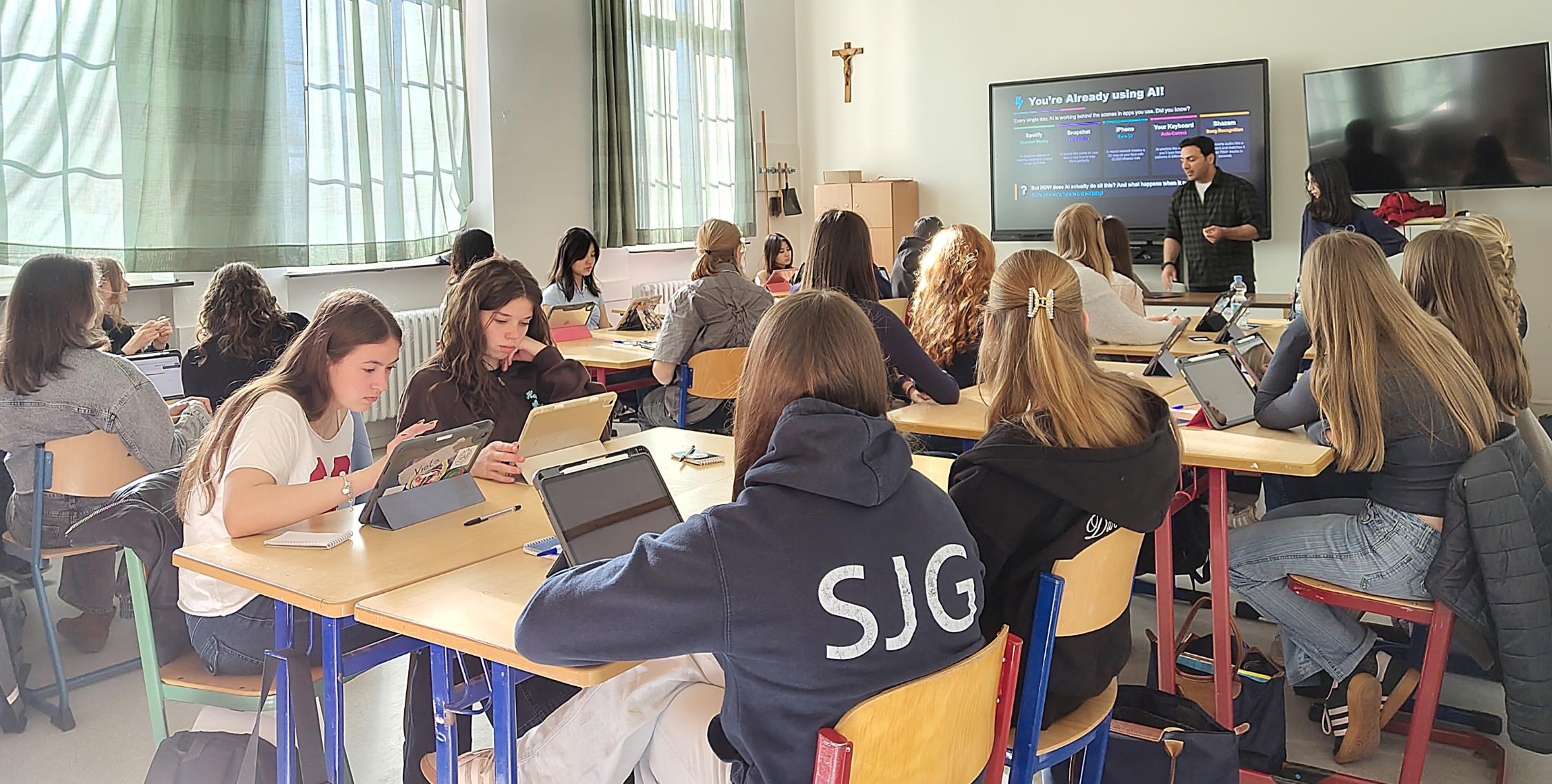 Schülerinnen in einem Klassenraum, Mann vor digitaler Tafel