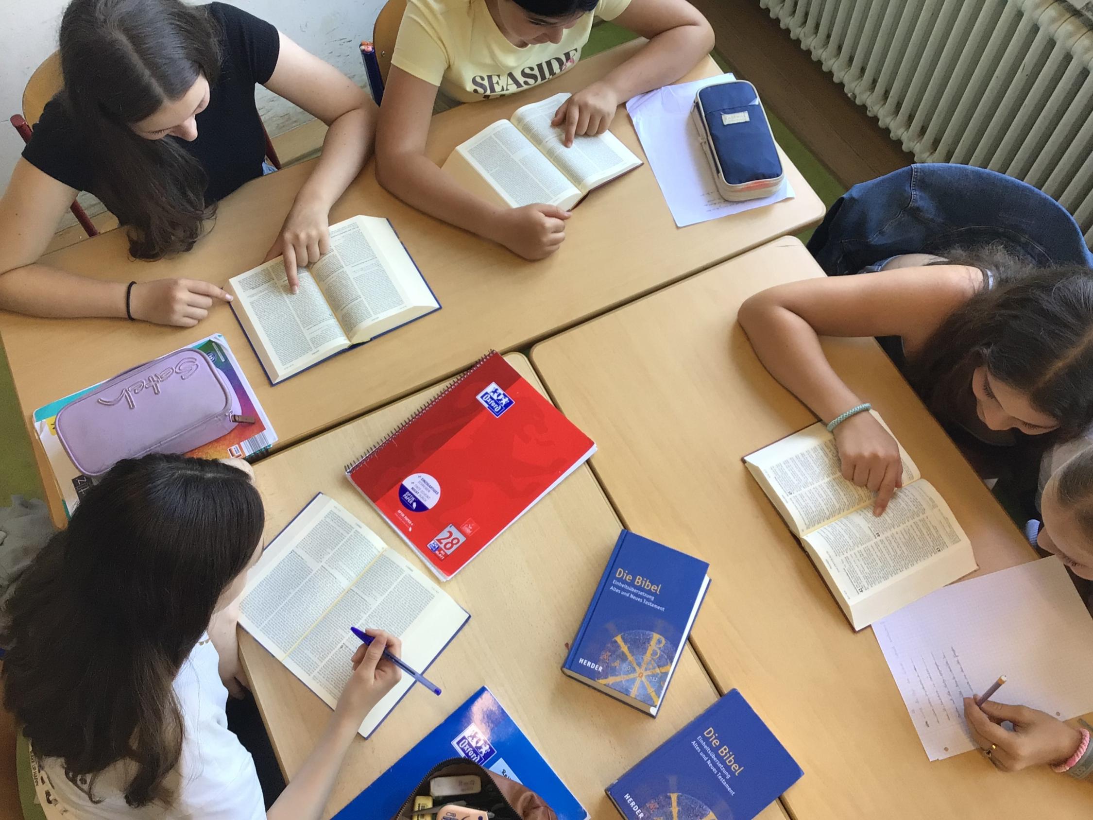 Schülerinnen lesen in der Bibel, sitzen am Gruppentisch