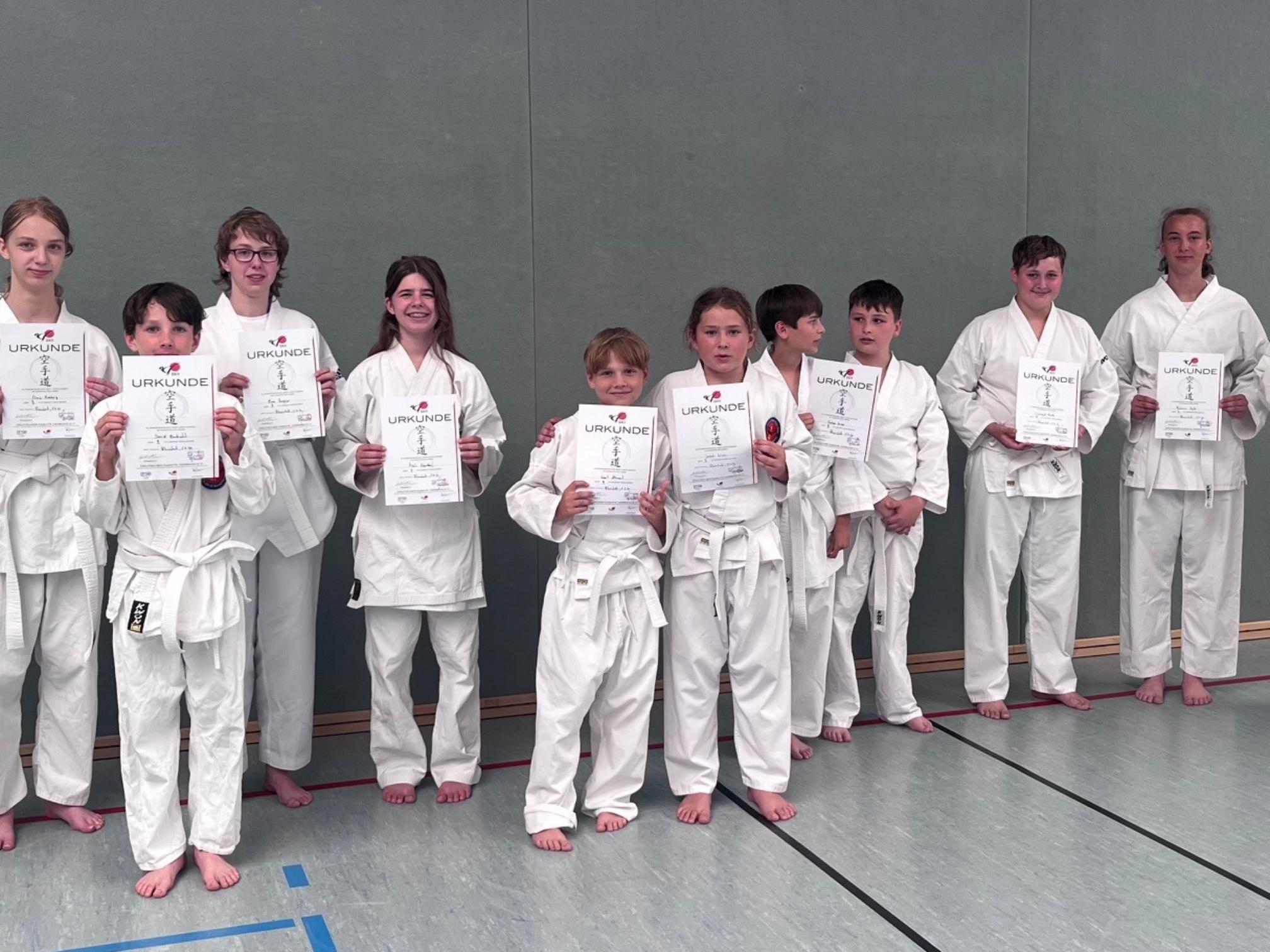 Jungen und Mädchen in Karate-Anzügen mit Urkunden in der Hand