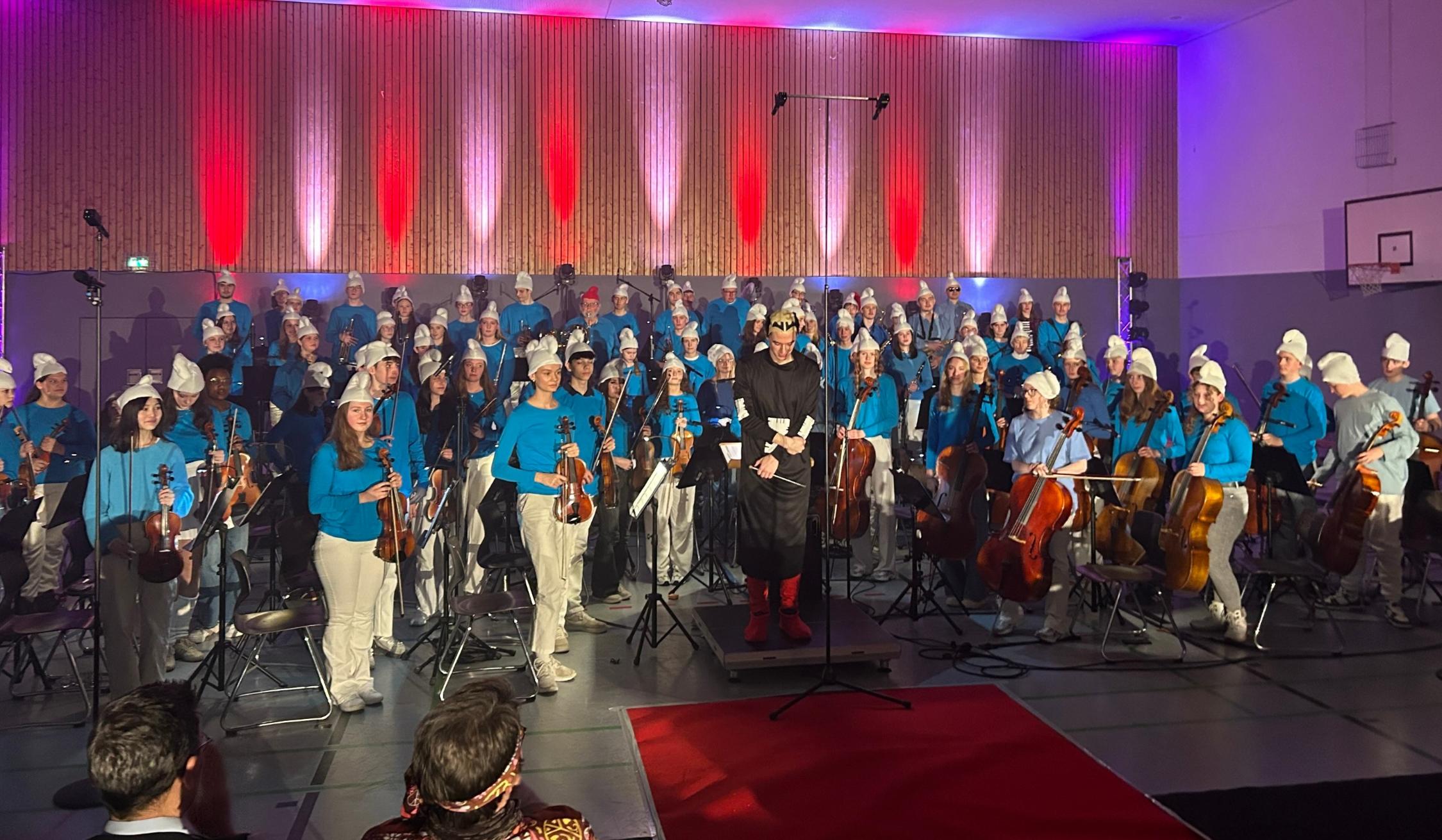 Orchestermitglieder im Schlumpfkostüm stehen, vorne in der Mitte Dirigent