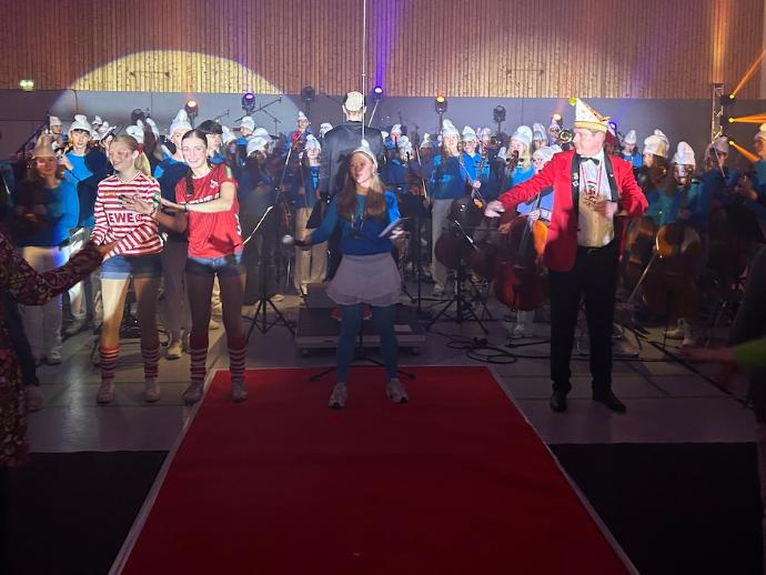 Hinten das Orchester, vorn kostümierte Schülerinnen und ein Herr tanzen