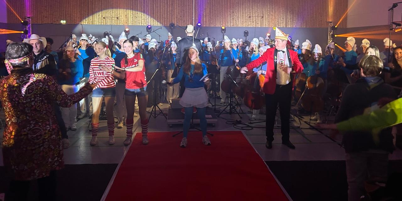 Hinten das Orchester, vorn kostümierte Schülerinnen und ein Herr tanzen