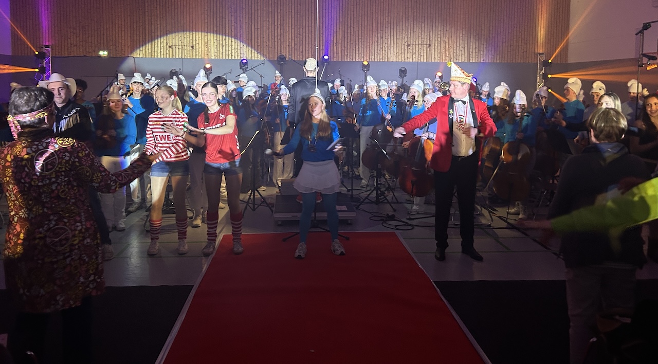 Hinten das Orchester, vorn kostümierte Schülerinnen und ein Herr tanzen