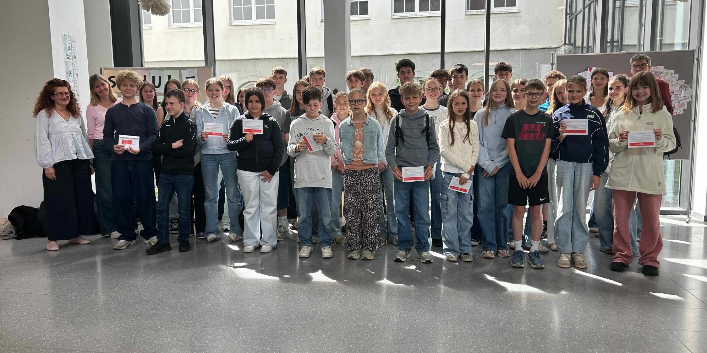 Gruppenbild mit Mädchen und Jungen, die Umschläge in den Händen halten, im Foyer der Schule