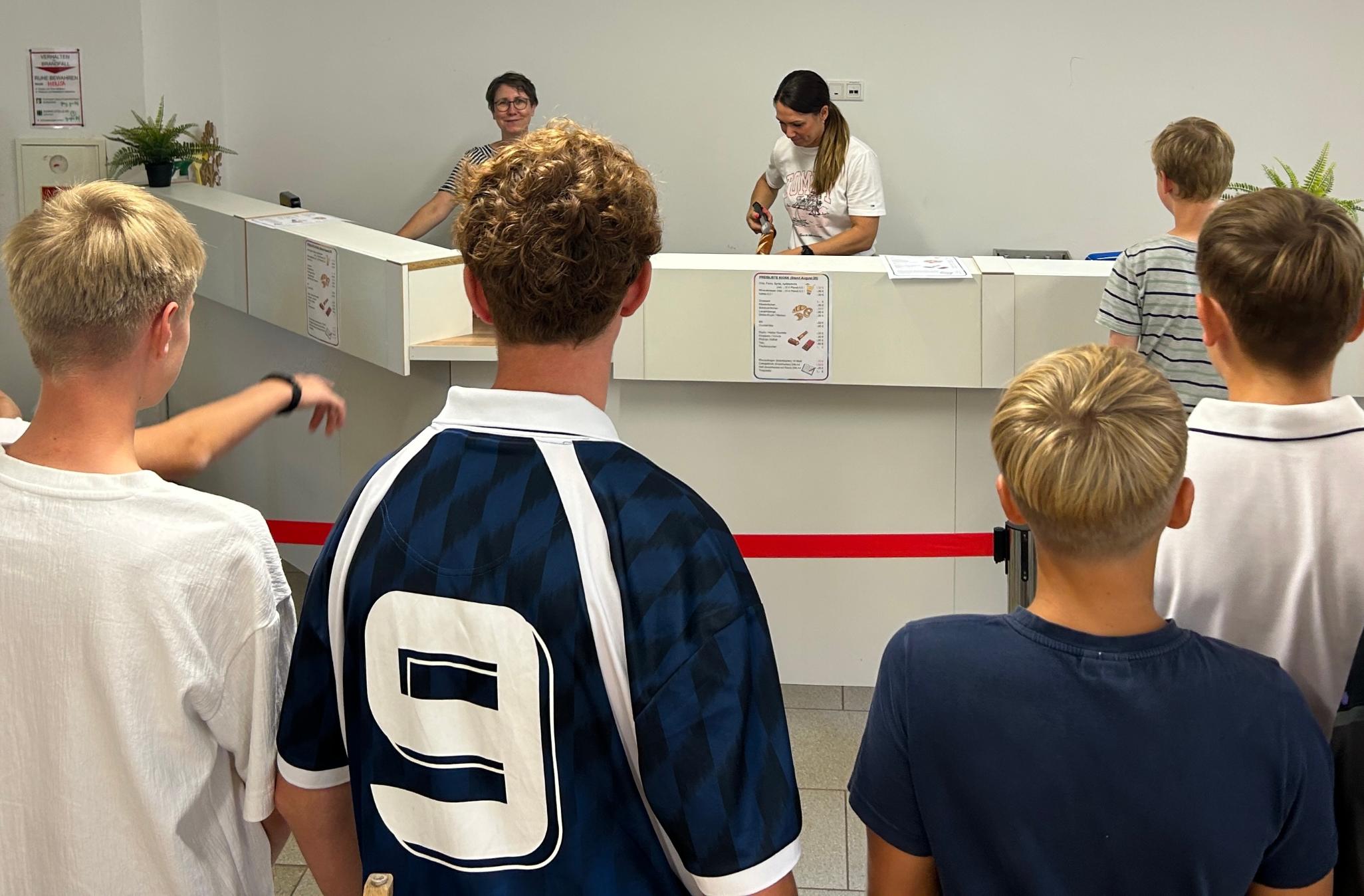 Schüler warten an der Theke, dahinter zwei Frauen