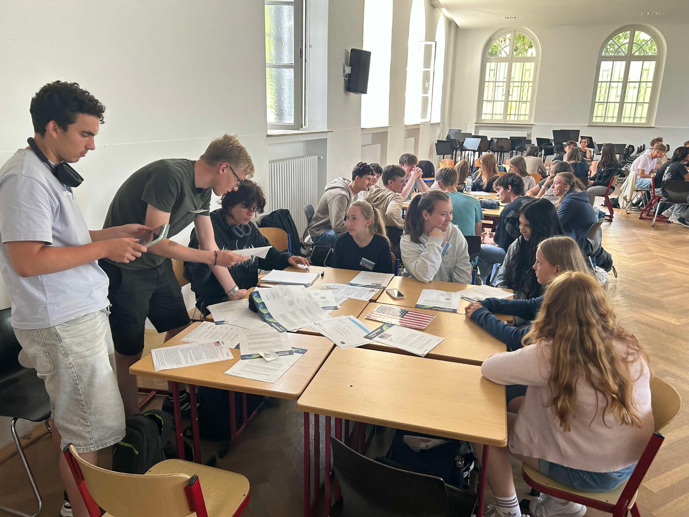 Schülerinnen und Schüler an Gruppentischen, über viel Material (Papier) gebeugt