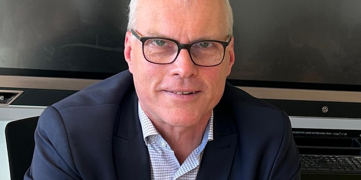 Mann sitzt im Klassenraum vor digitaler Tafel