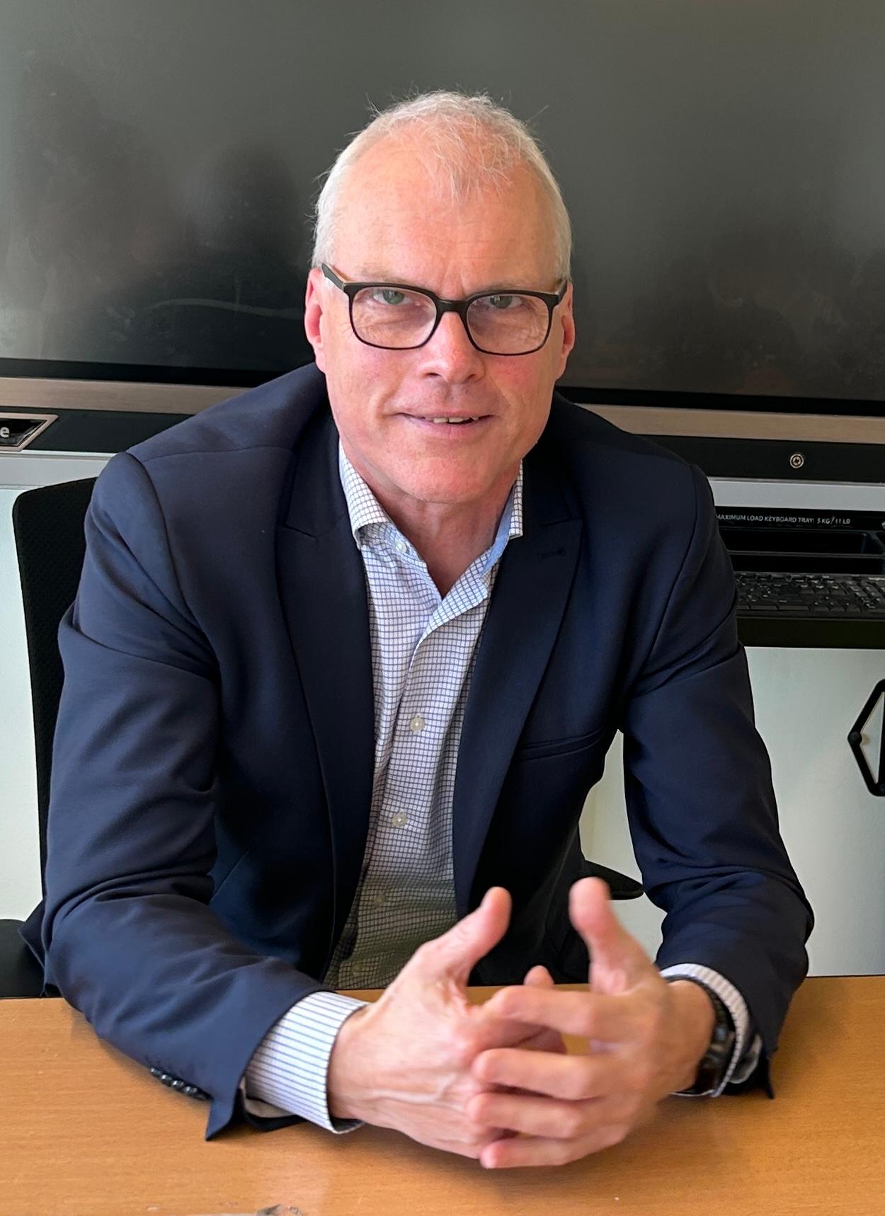 Mann sitzt im Klassenraum vor digitaler Tafel