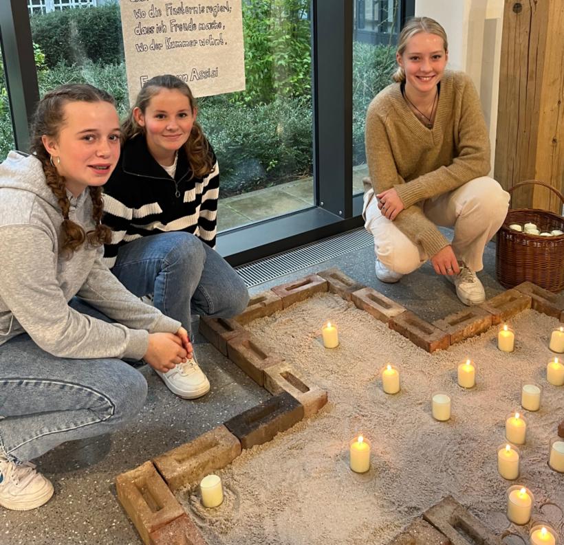 Schülerinnen vor einem Kreuz mit Kerzen im Foyer