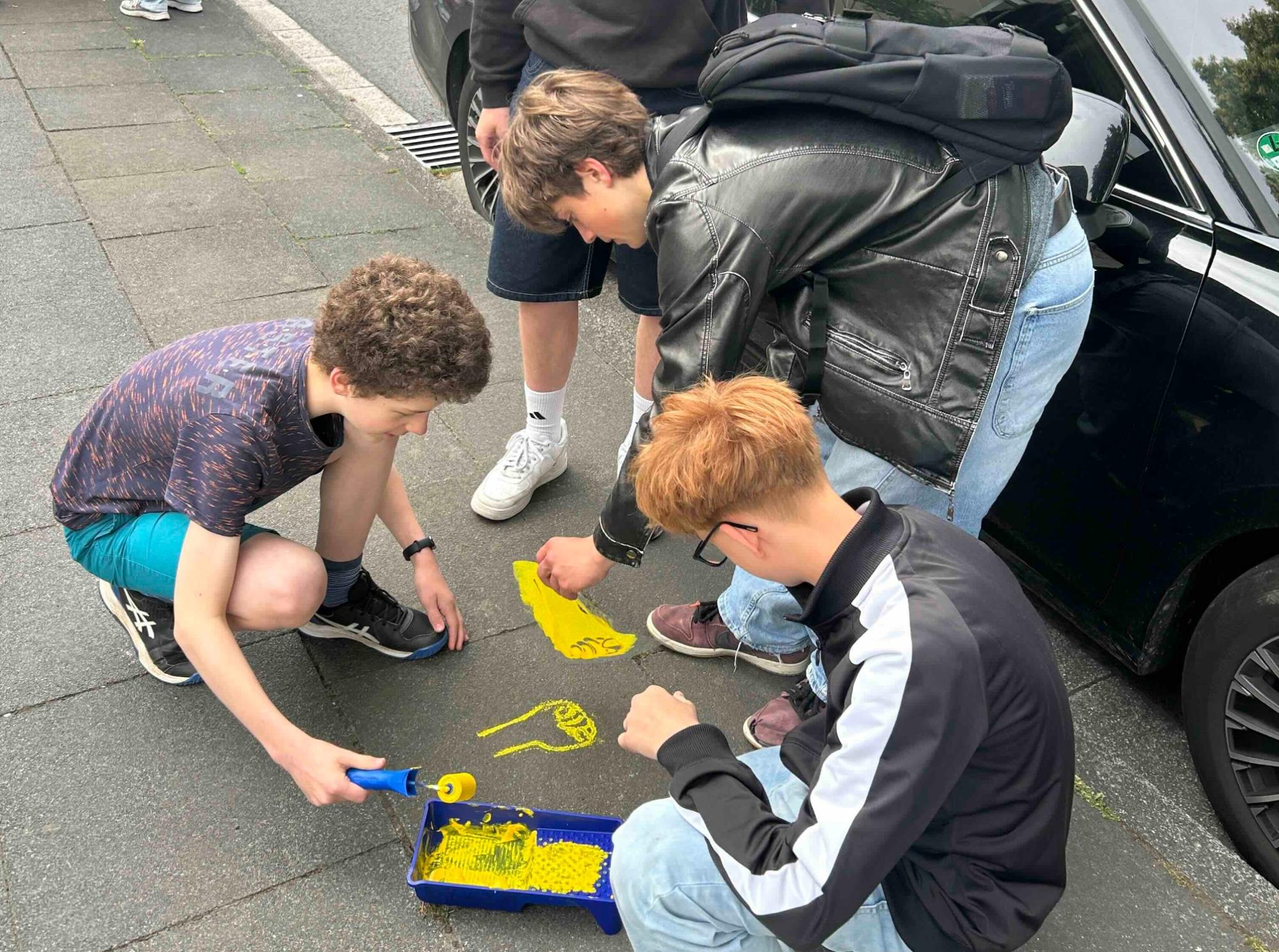 Schüler tragen Farbe auf eine Schablone auf, andere Schüler schauen zu