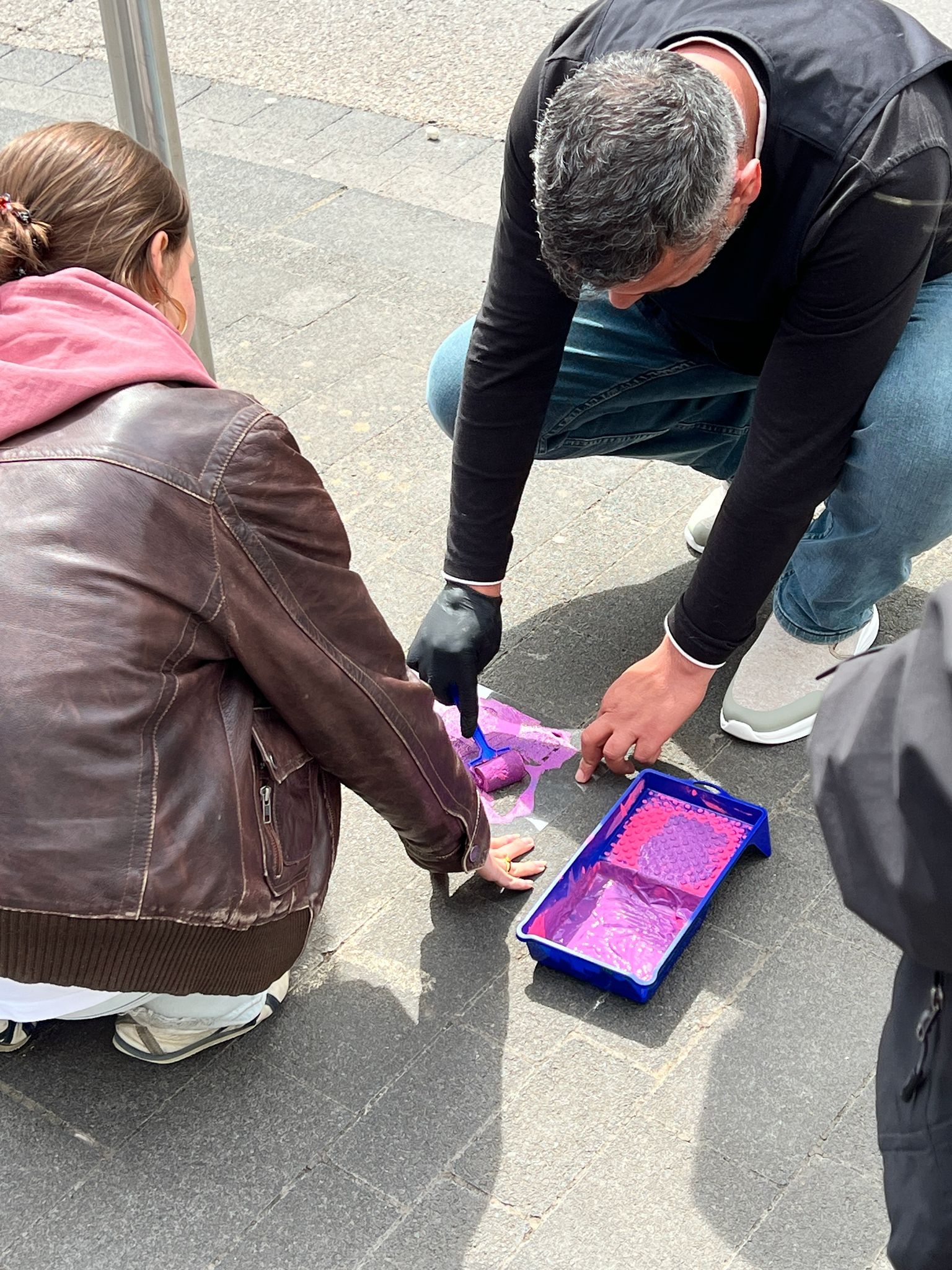 zwei Menschen tragen mit Farbe und Schablone ein Symbol auf dem Gehweg auf