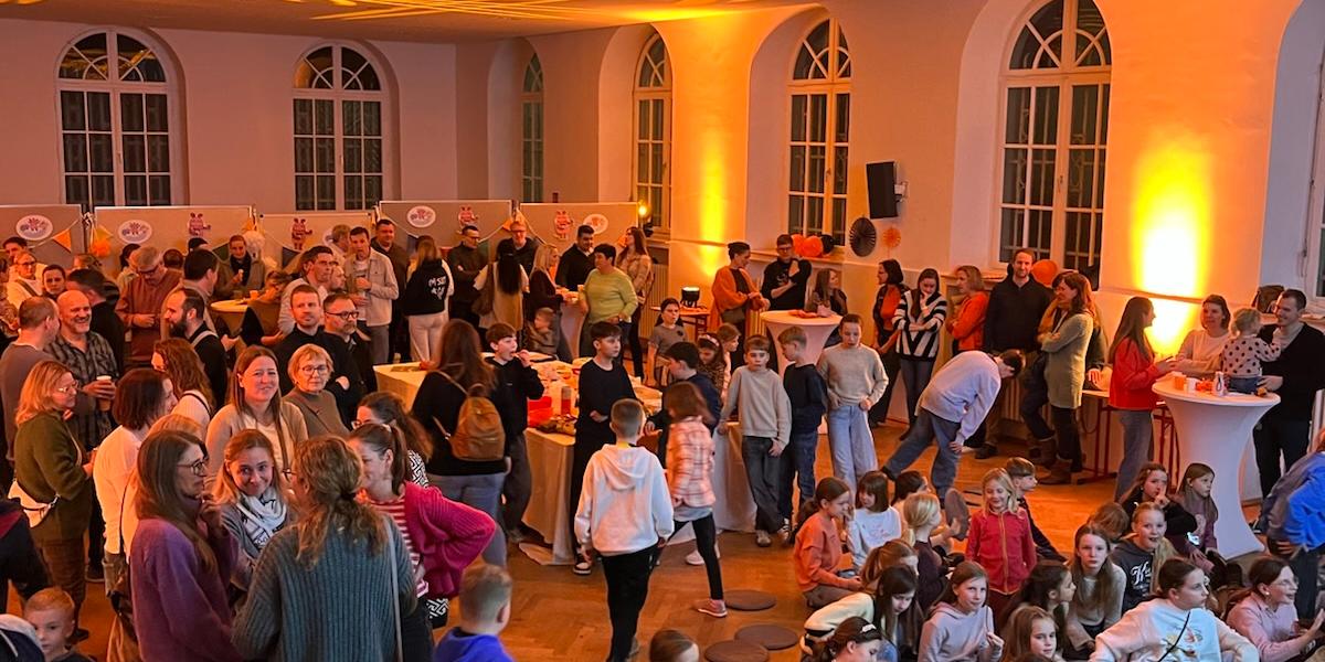 Kinder und Erwachsene stehen mit Blick auf eine digitale Tafel im orange beleuchteten Raum
