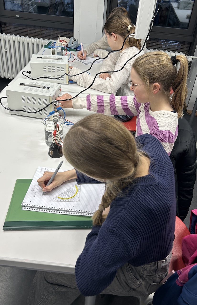 drei Schülerinnen vor einem Wechselstromgerät,  eine Schülerin notiert Werte