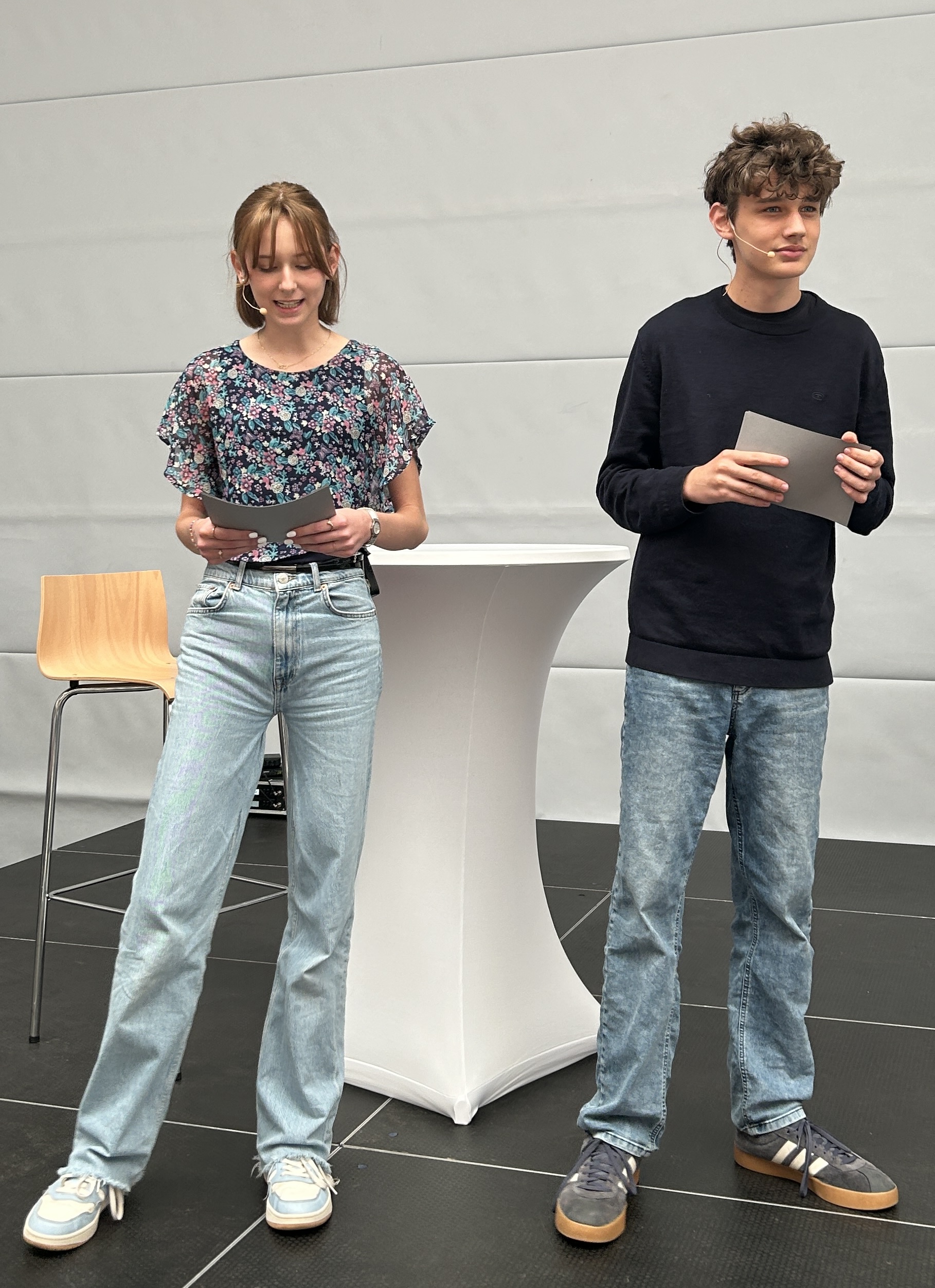 ein Mädchen, ein Junge, beide mit Karteikarten in der Hand, vor einem Stehtisch