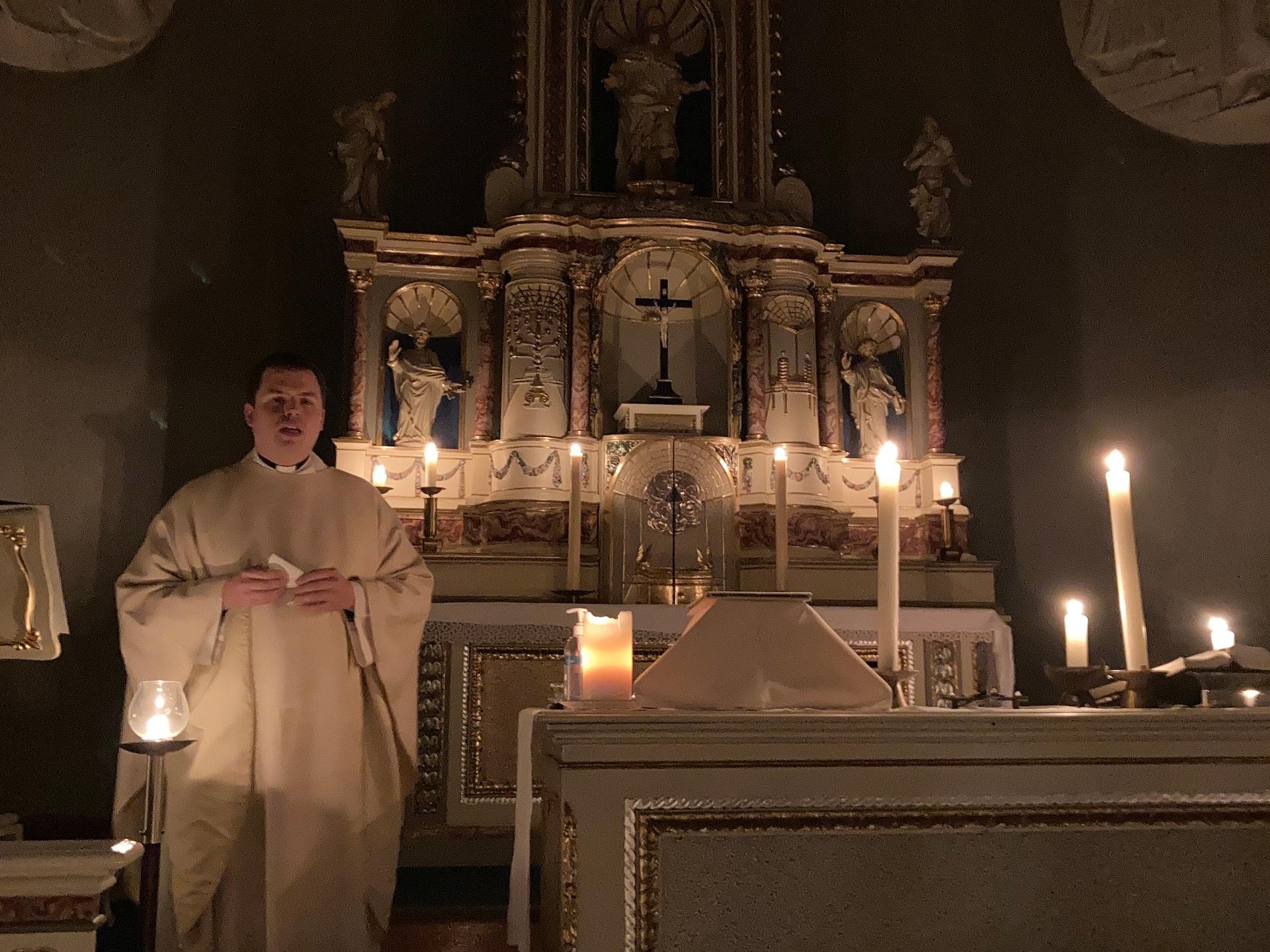 Priester vor mit Kerzen erleuchtetem Altar