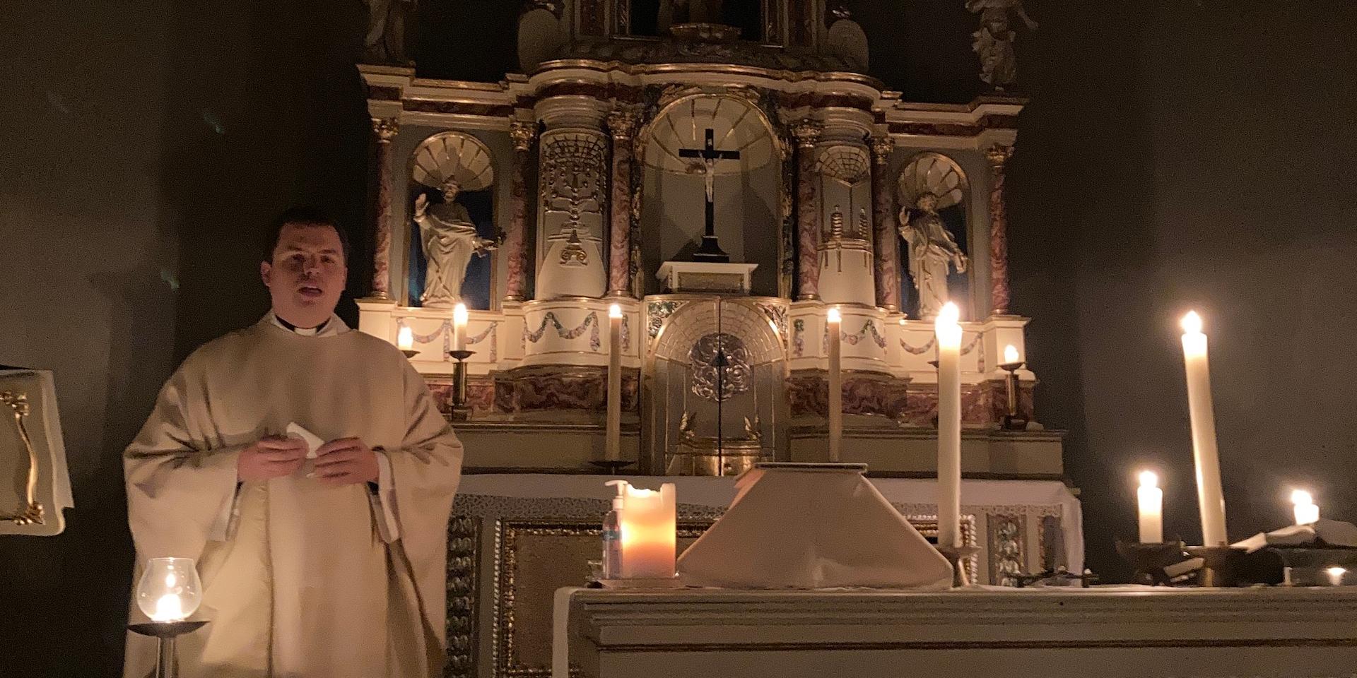 Priester vor mit Kerzen erleuchtetem Altar