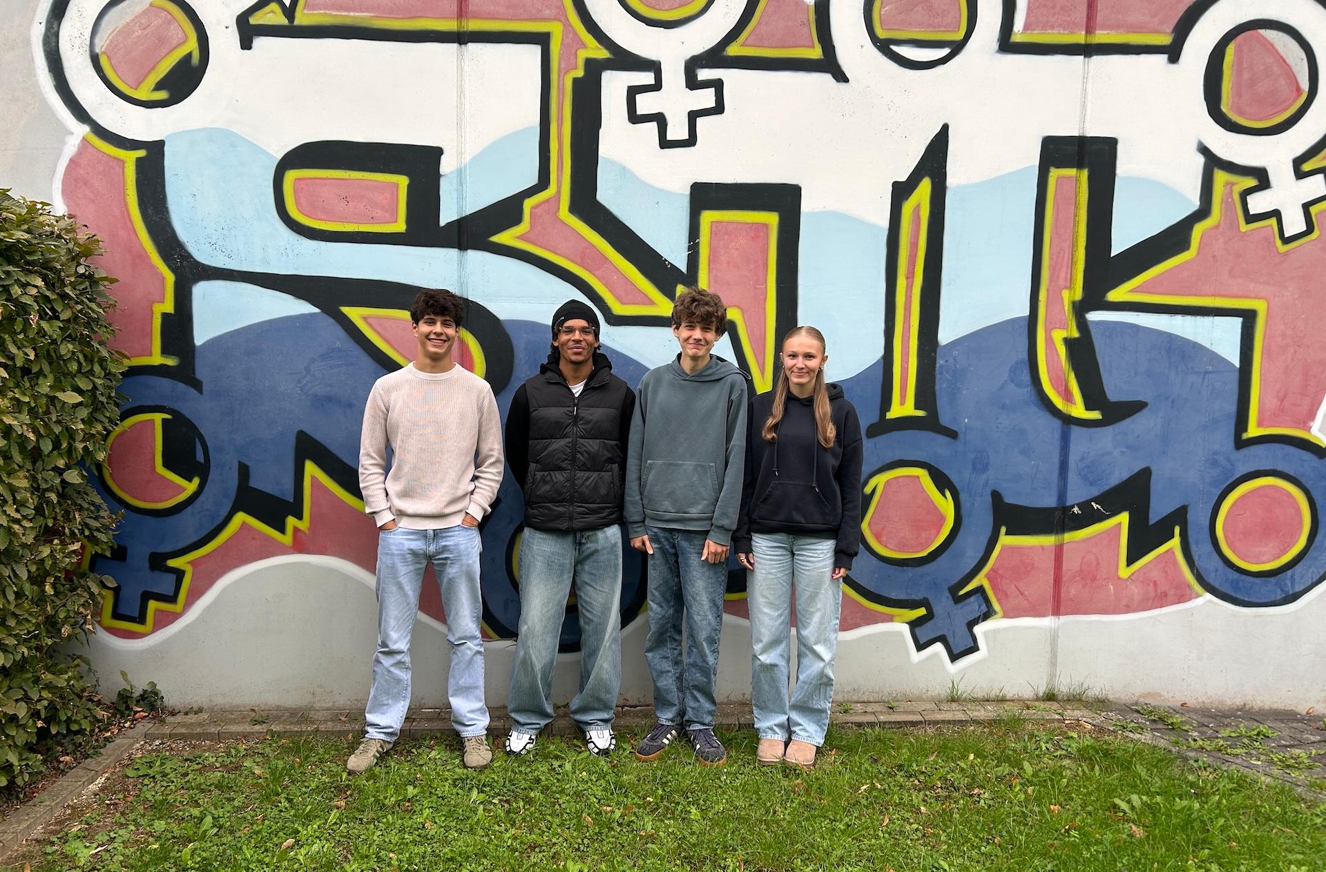 drei Jungen, ein Mädchen vor einem Graffiti mit den Buchstaben SJG
