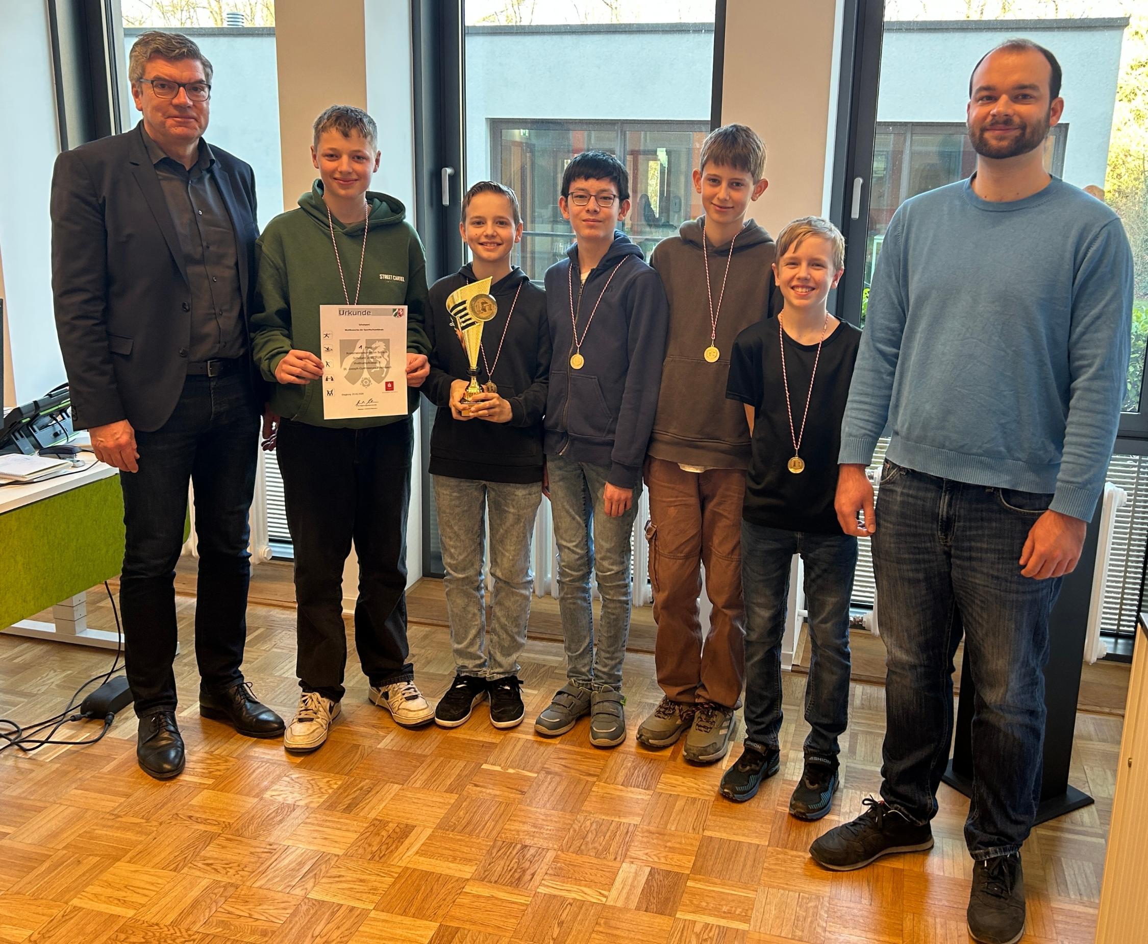 Gruppenbild: fünf Jungen, am Rand zwei Männer, ein Junge hält eine Urkunde und einer einen Pokal in den Händen