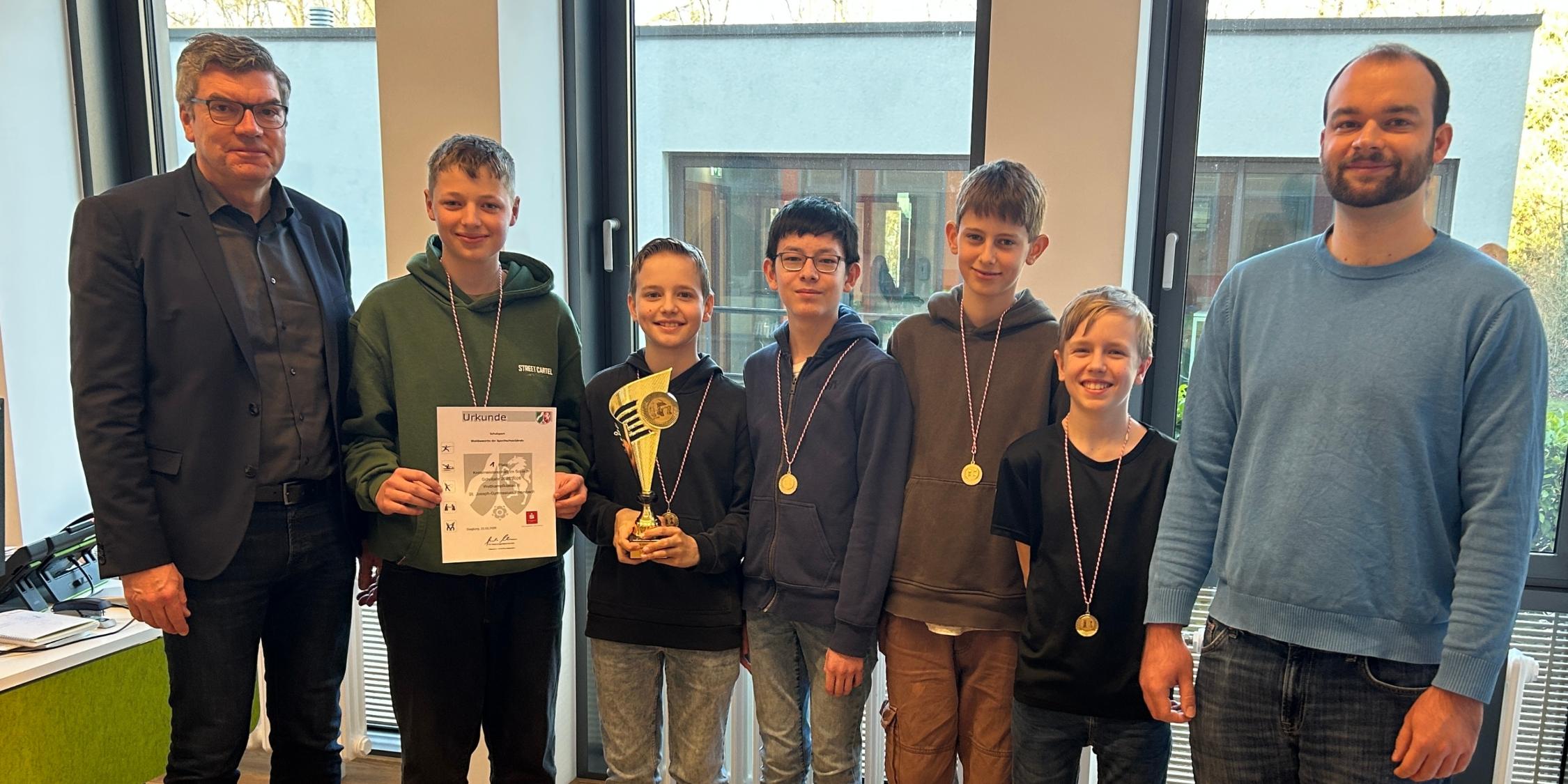 Gruppenbild: fünf Jungen, am Rand zwei Männer, ein Junge hält eine Urkunde und einer einen Pokal in den Händen