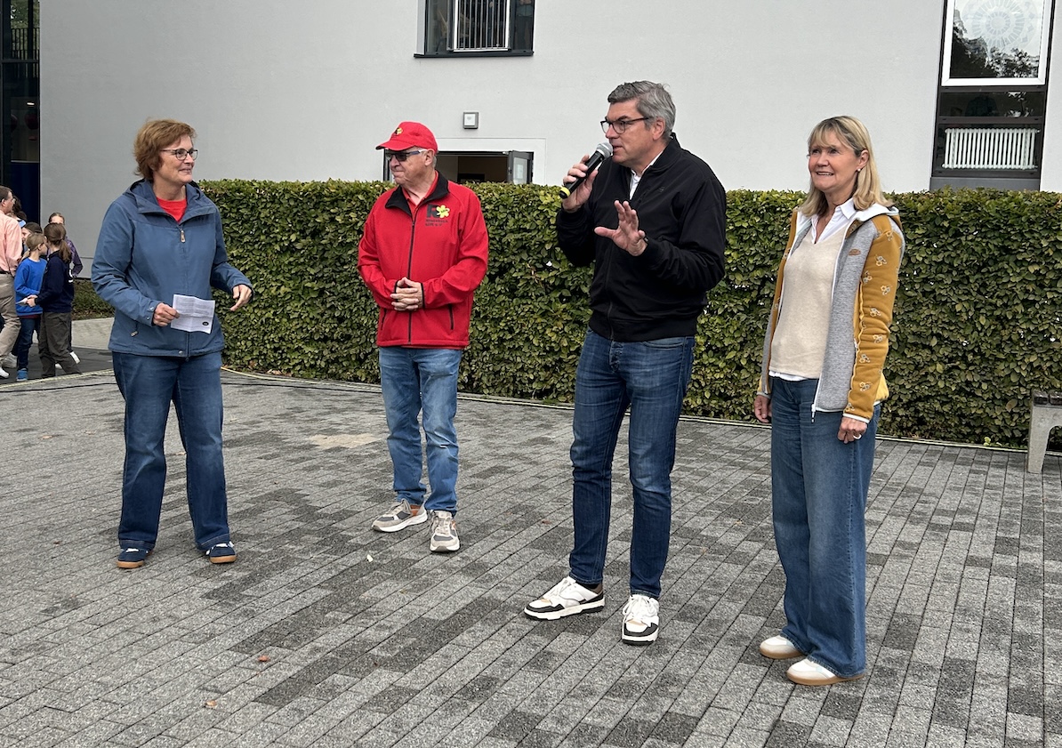 Mann (Schulleiter) spricht ins Mikro, rechts eine Frau (stv. Schulleiterin), links Mann und Frau